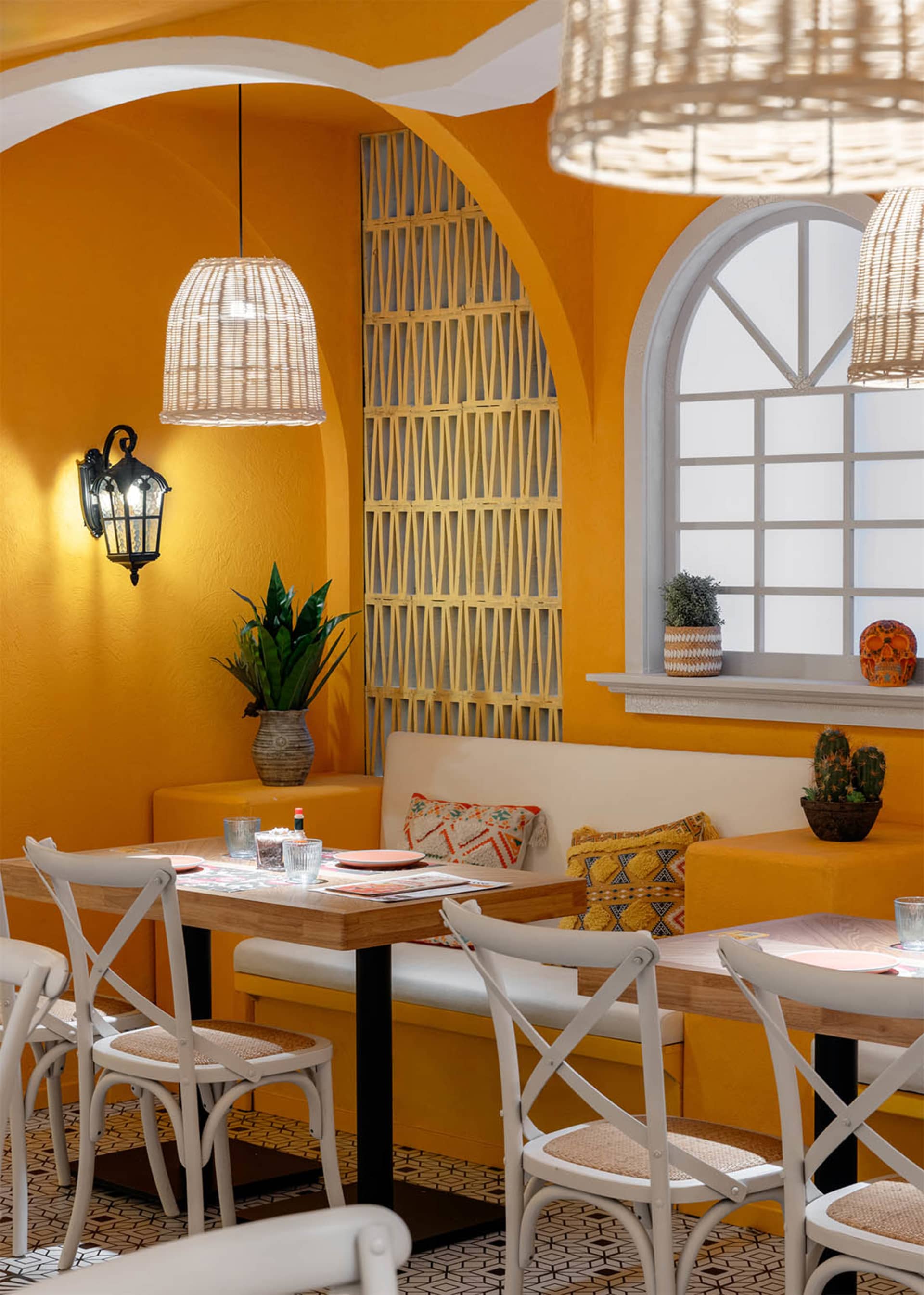 Warm and inviting dining room with a yellow wall, a wooden table, and comfortable seating, surrounded by potted plants and decorative vases