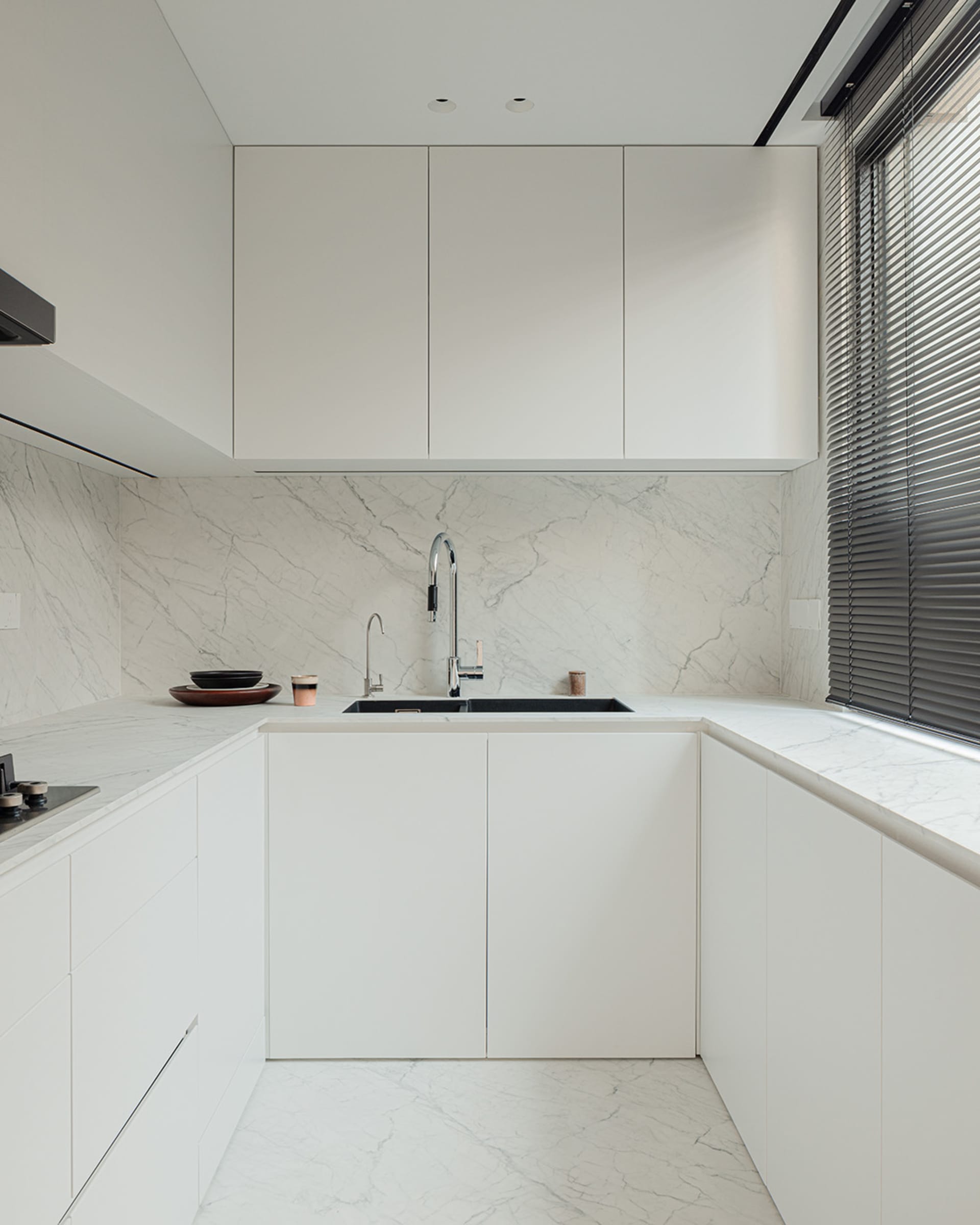 A modern kitchen with white cabinets, marble countertops, a sink, a bowl, and a cup, lit by natural light