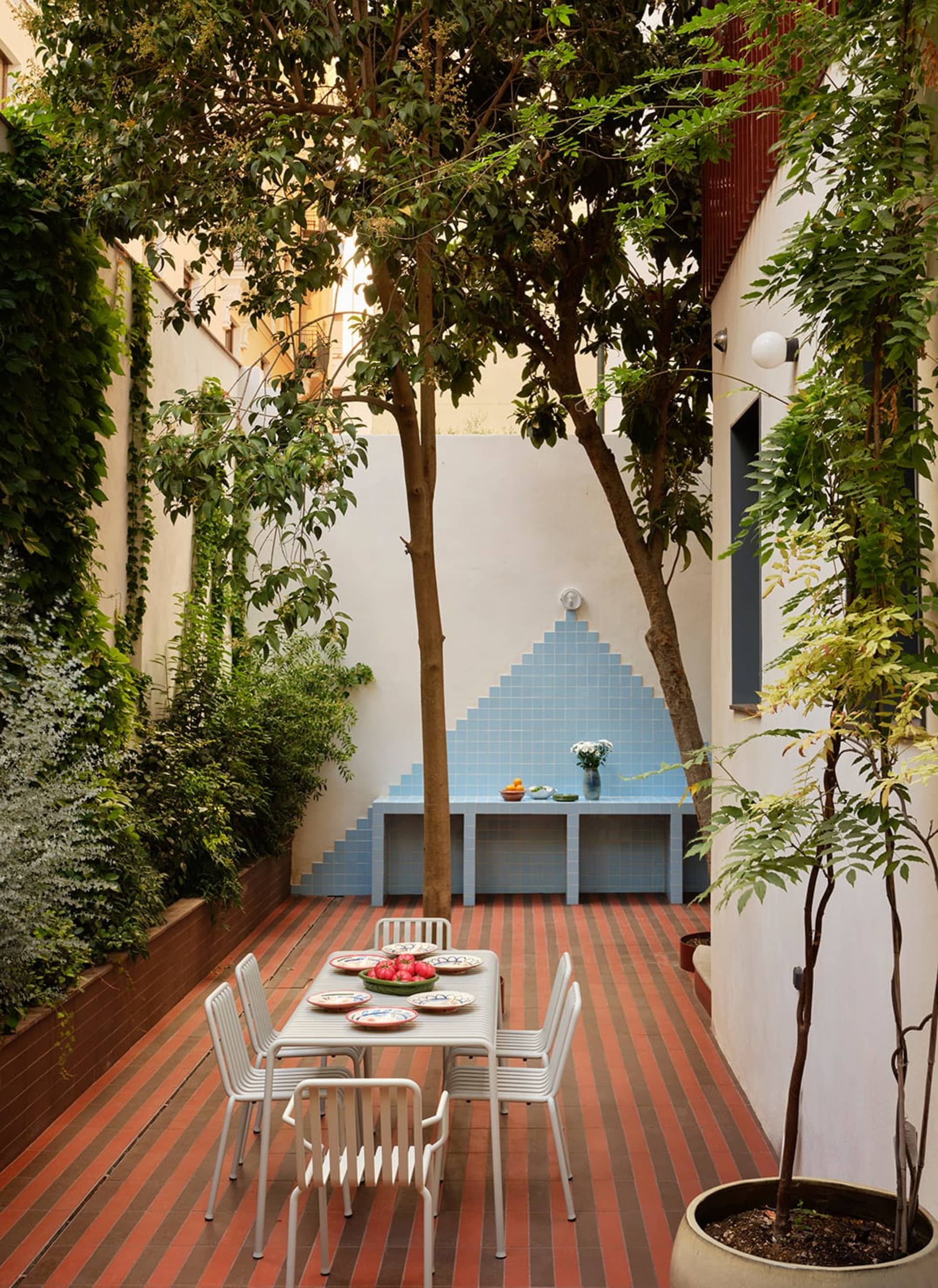 A patio dining area with a table set for a meal, surrounded by chairs and a bench, decorated with potted plants