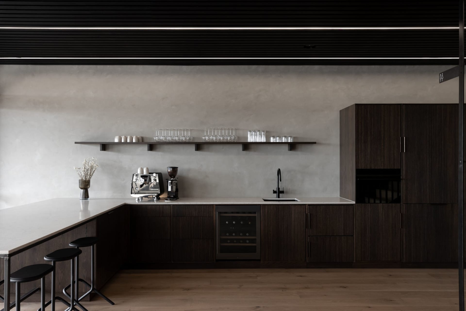 Modern kitchen with wooden cabinets, a black refrigerator, and dim lighting, featuring a sink, microwave, coffee maker, and decorative items