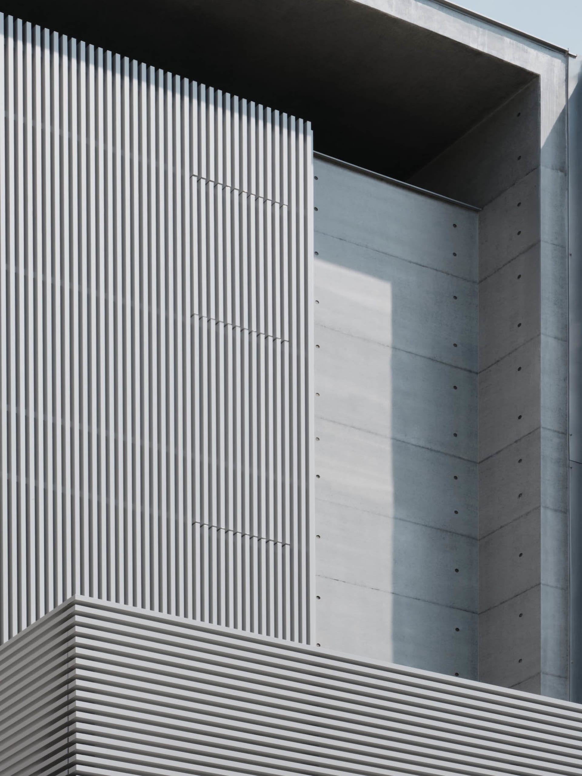 A modern building with a large concrete wall featuring a row of vertical stripes, set against a bright and sunny day