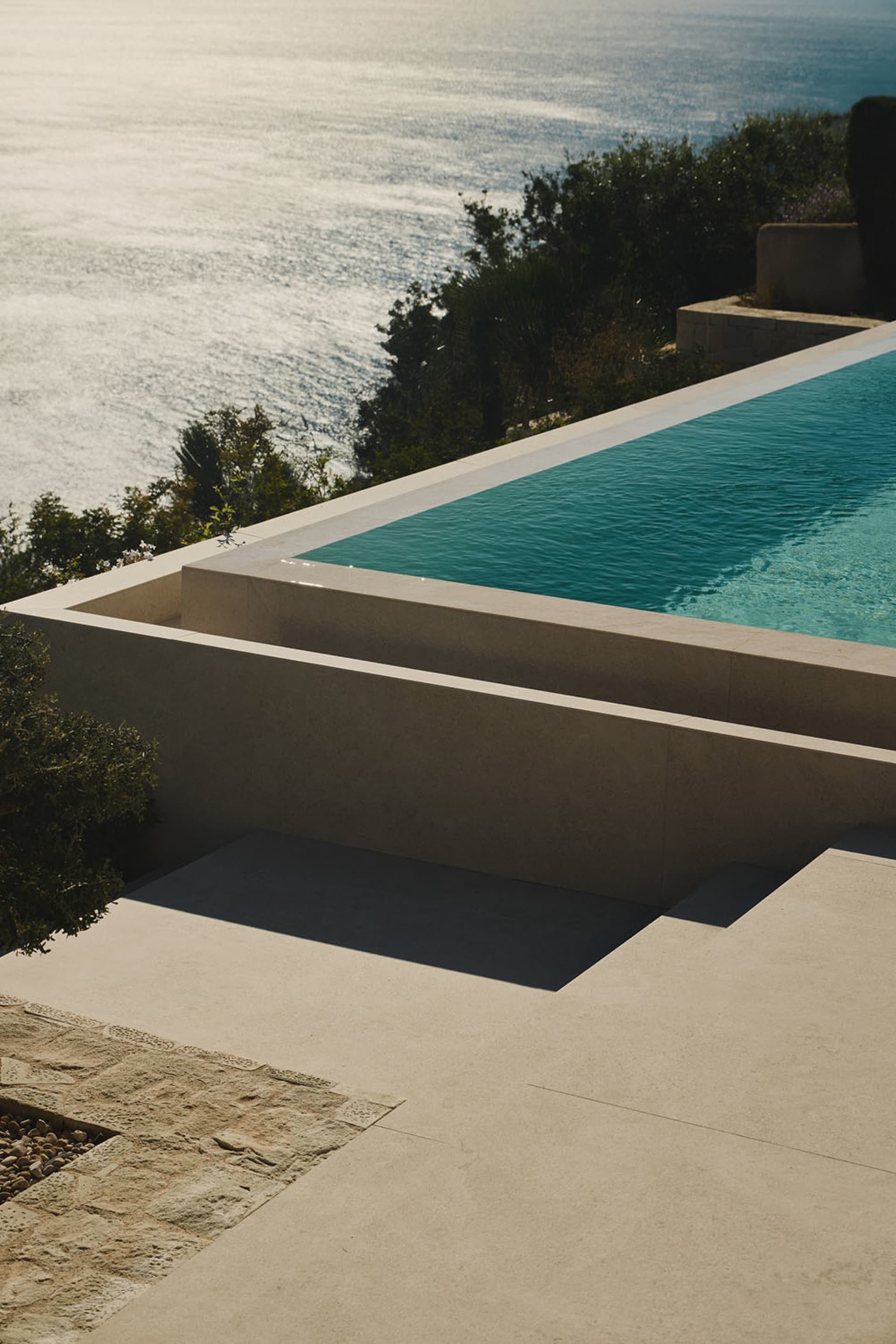 A large pool area with a blue pool surrounded by white walls and flooring, set on a hillside with a picturesque view of the surrounding landscape