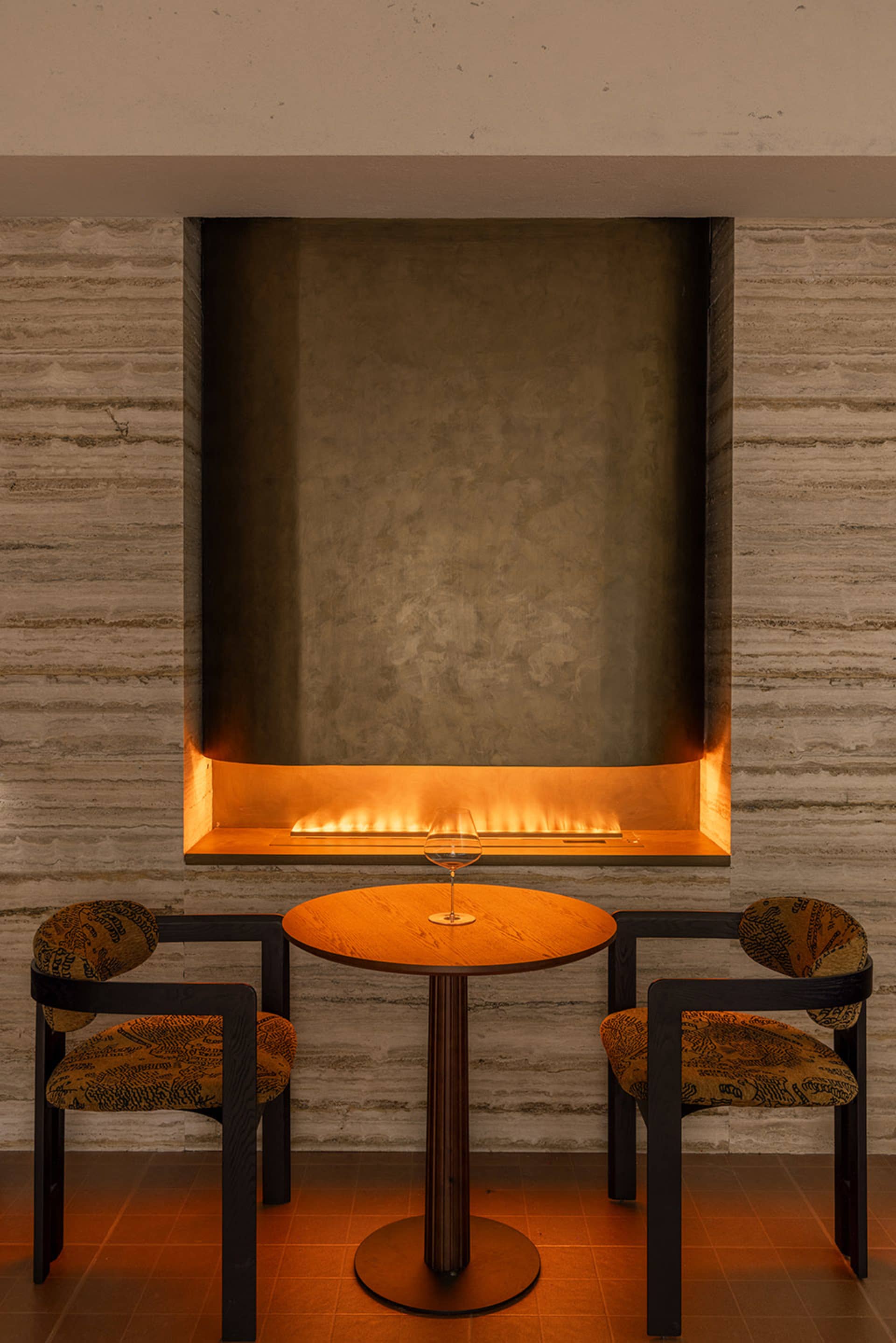 Cozy living room with a stone wall, a dining table, and chairs, featuring a fireplace and modern furniture