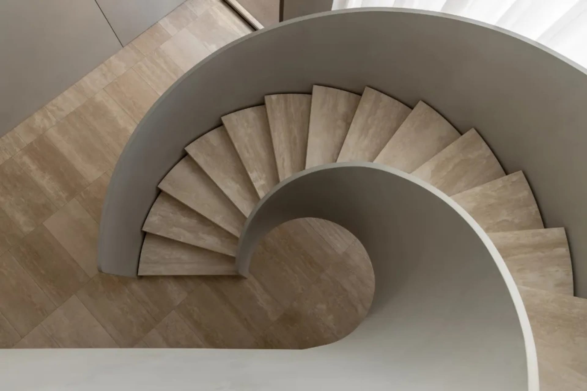 A spiral staircase in a room with a white floor and natural light, surrounded by a calm and inviting atmosphere