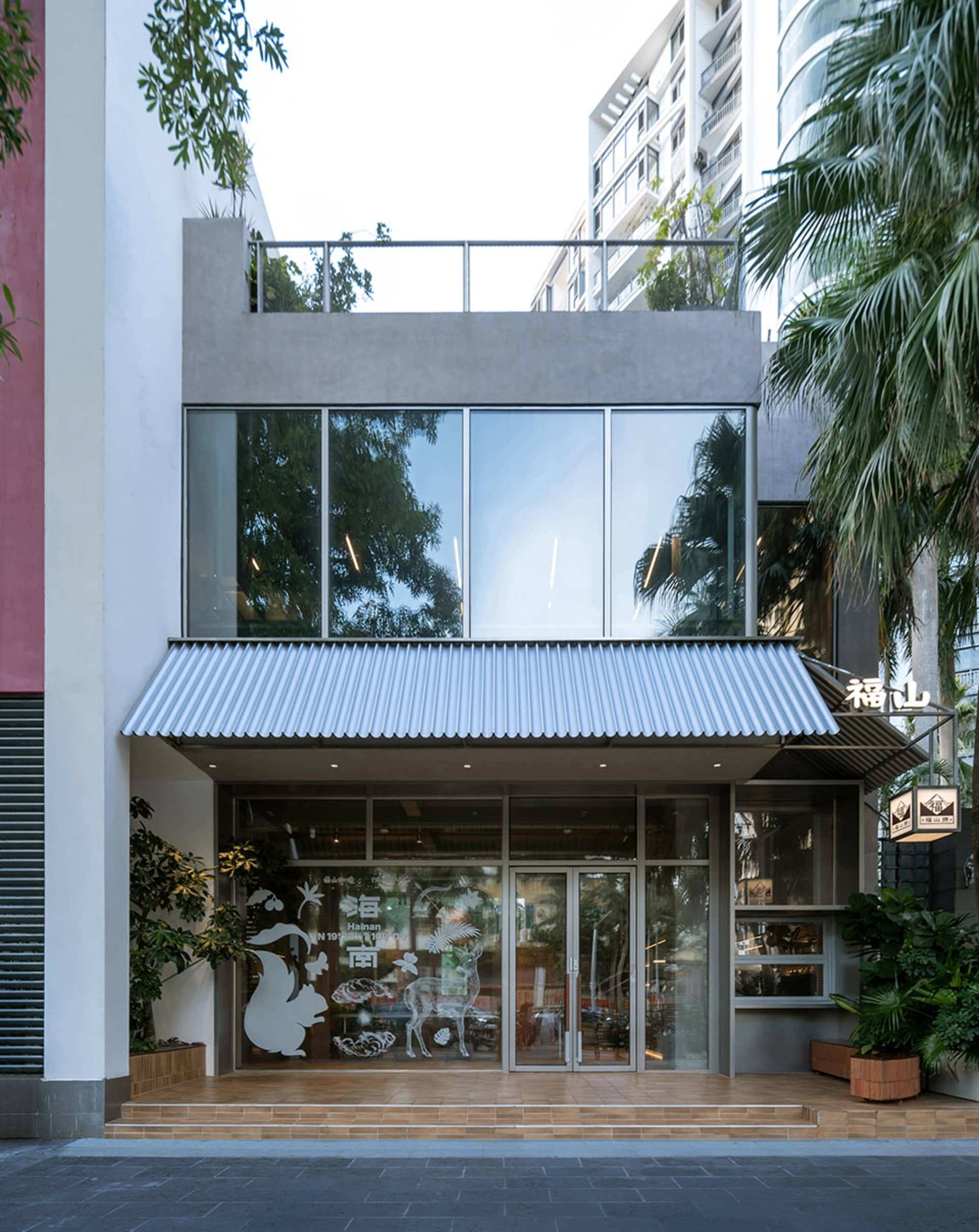A commercial office building with a modern glass front, featuring a large window and metal awning, bathed in natural light