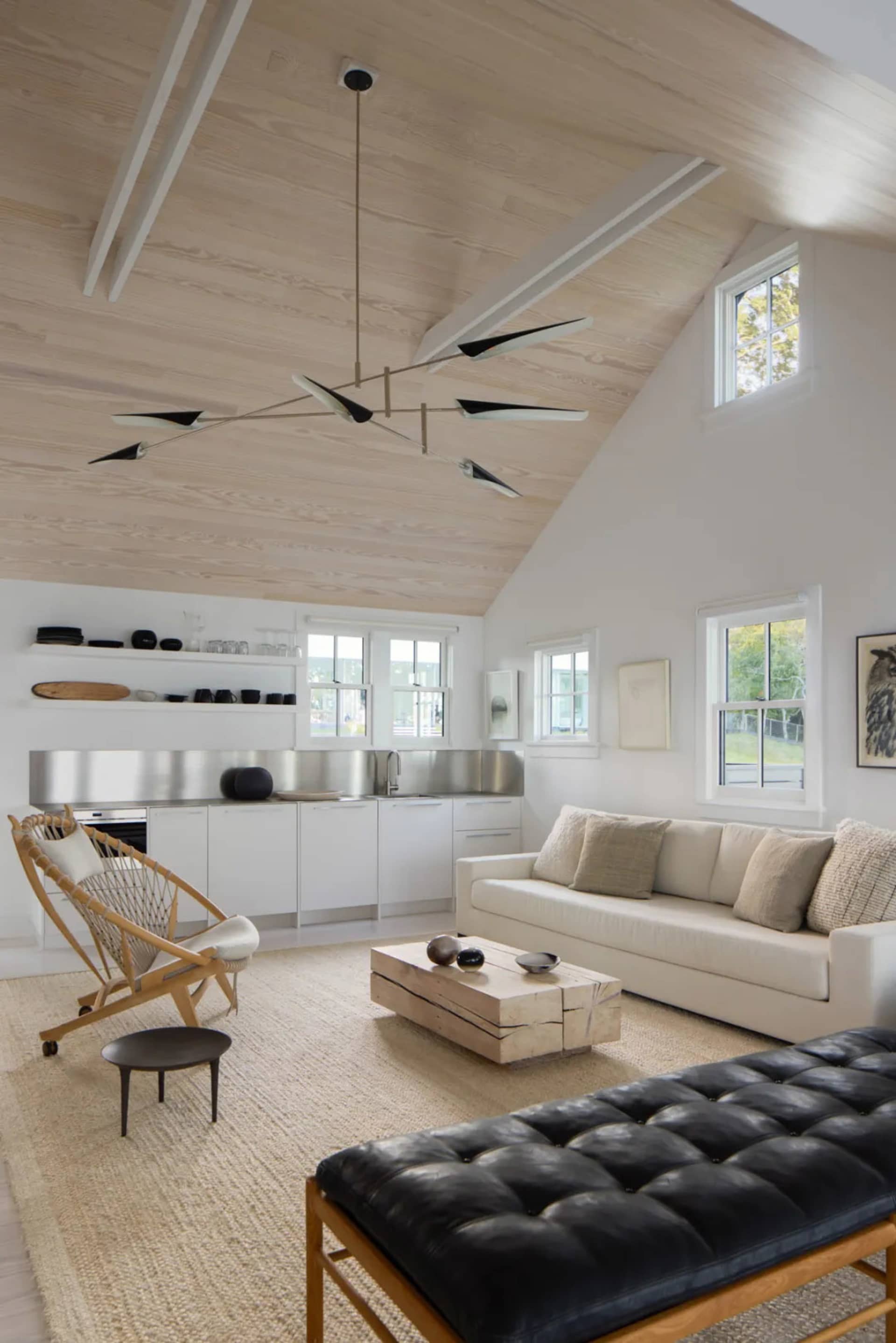 A modern living room with a white couch, chair, and dining table, featuring a kitchen area and natural light from windows