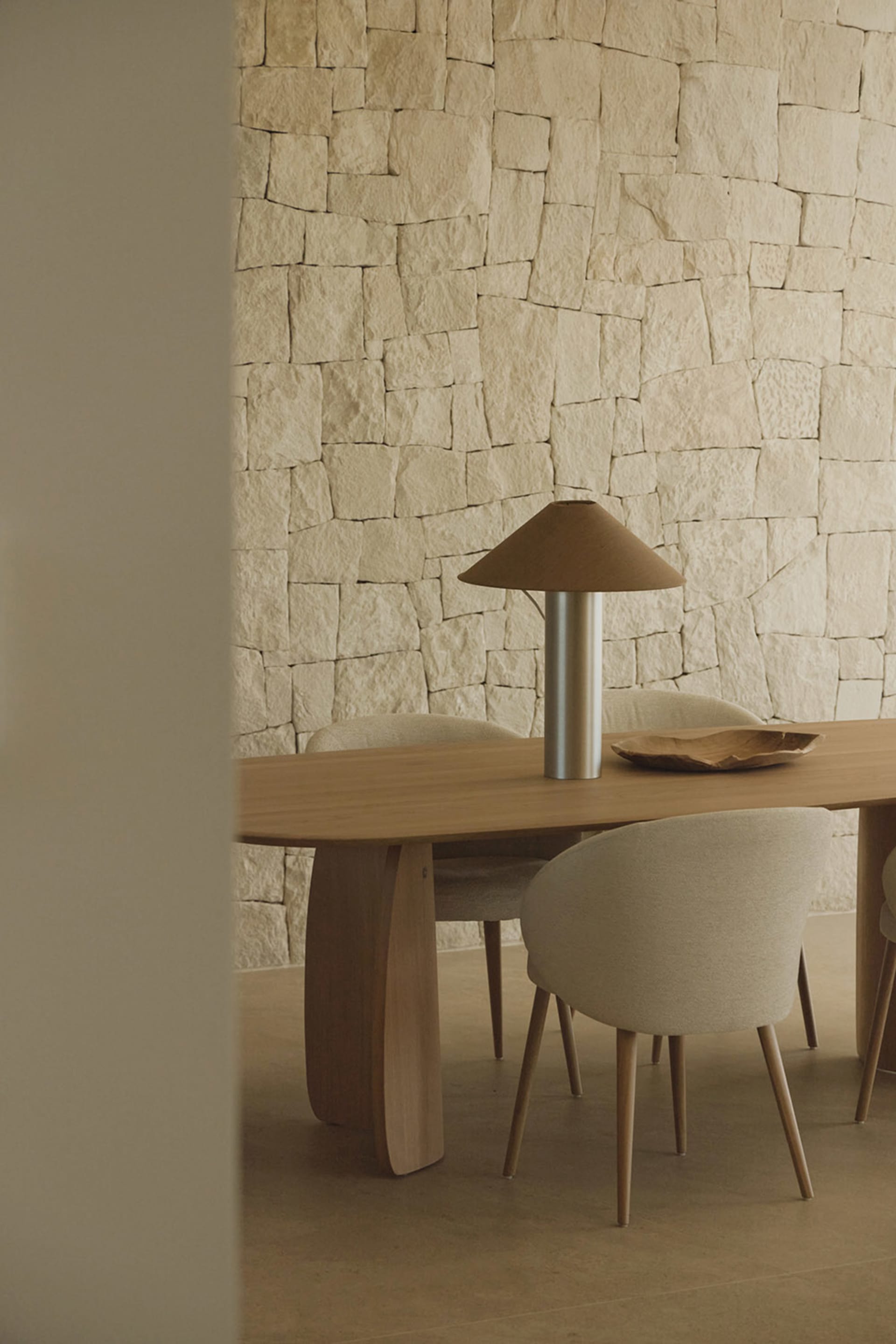 A modern dining room with a wooden table and chairs surrounded by a stone wall, well-lit and inviting