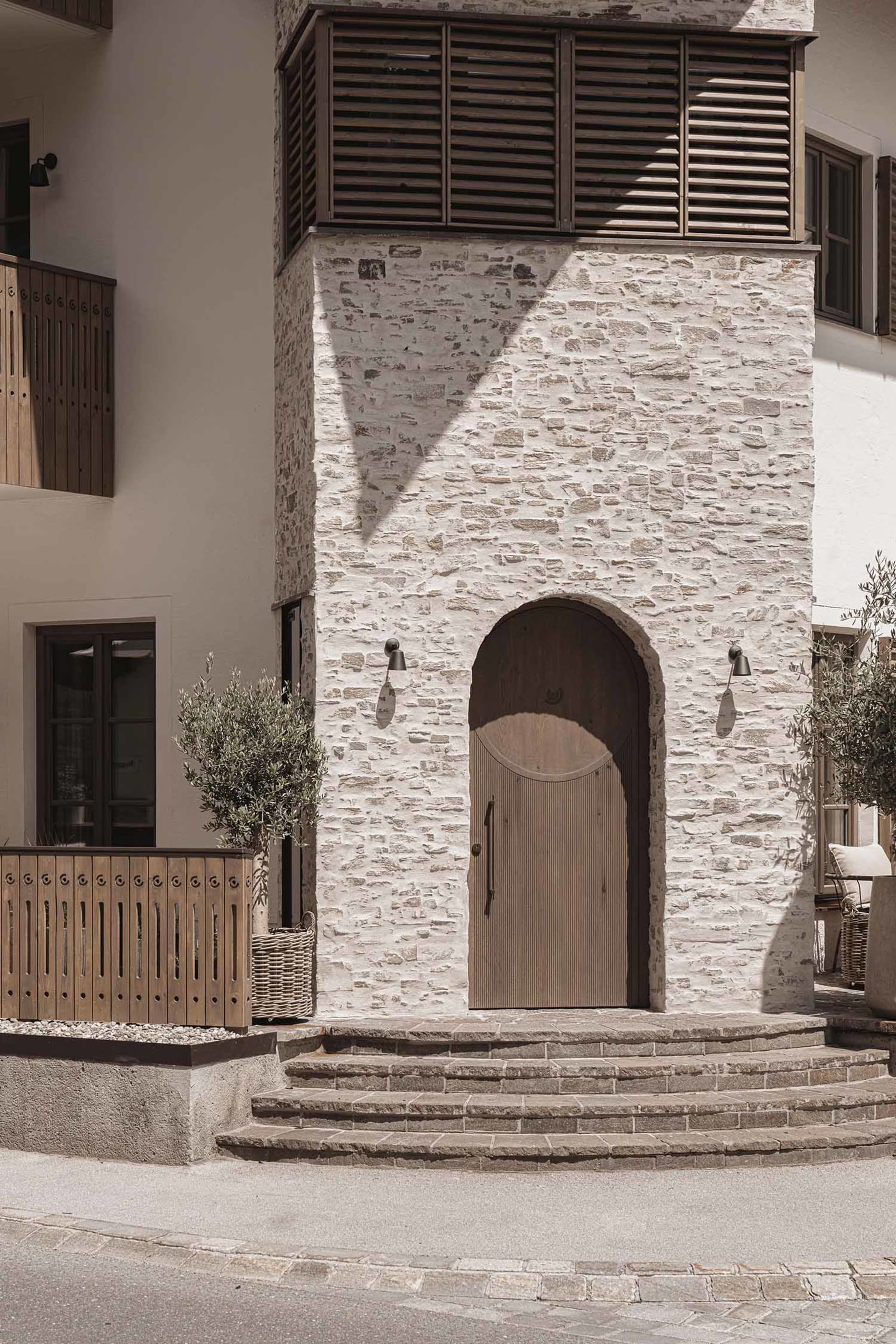 A modern building with a traditional stone archway and wooden door, featuring a brick-like appearance and natural lighting