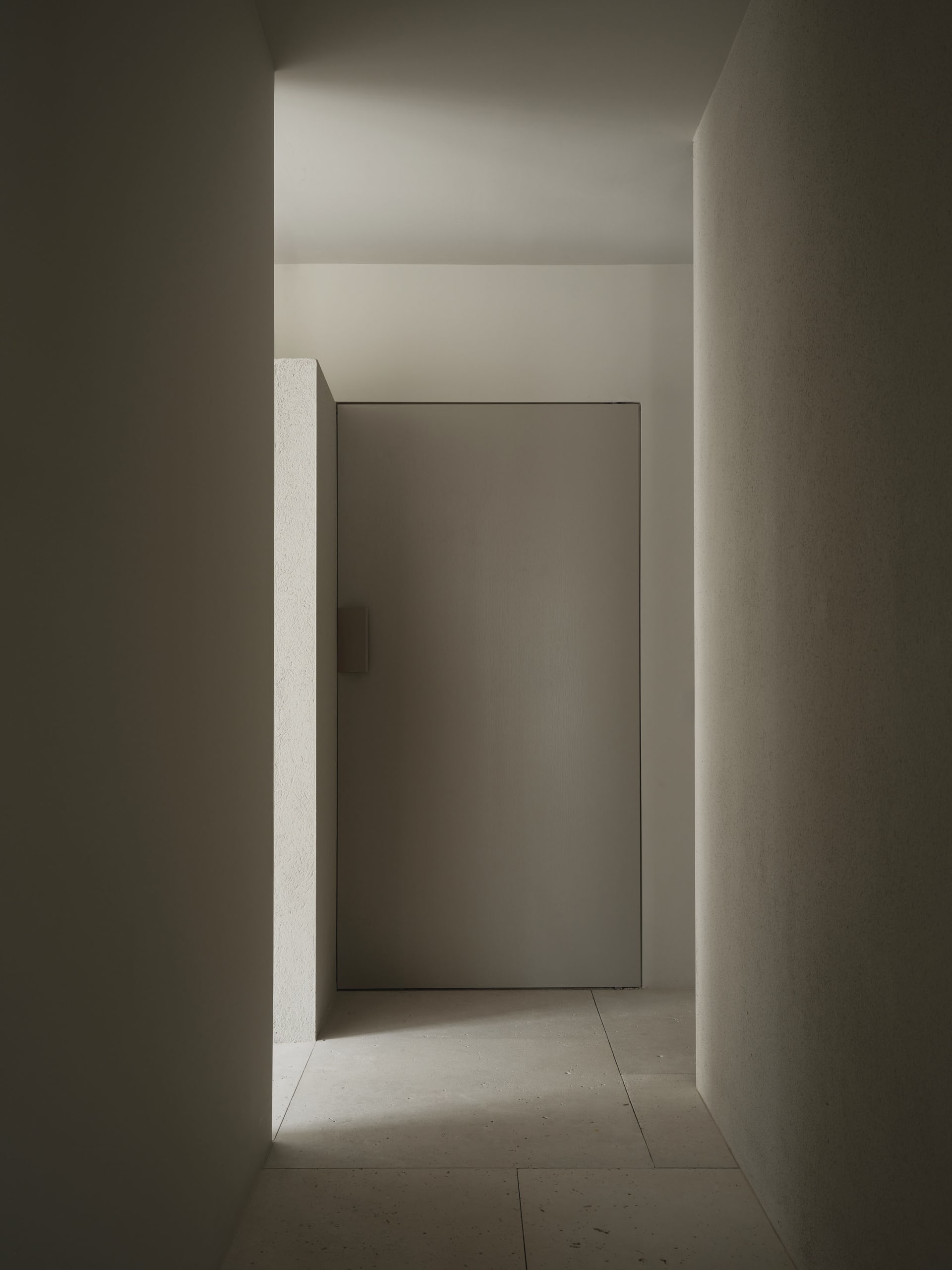 A dimly lit concrete hallway with a white door open to reveal the interior of the building