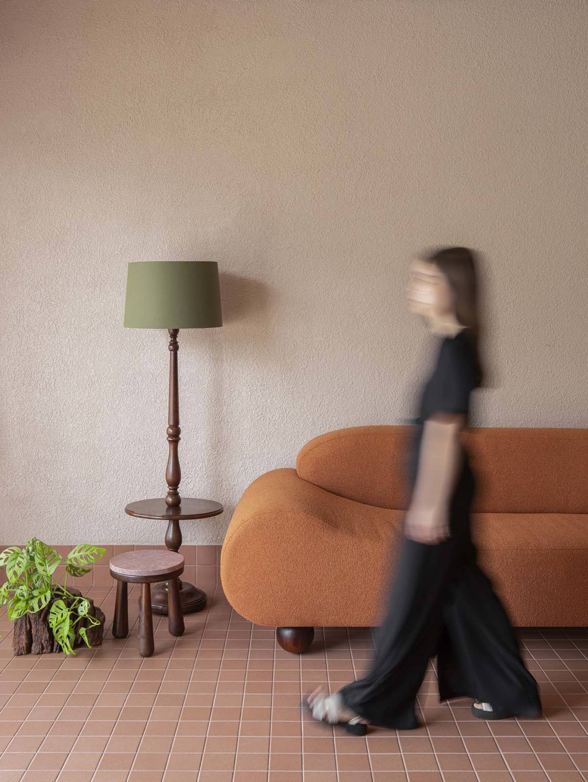 A woman walks towards a couch in a warm and inviting living room with brown furniture and natural lighting