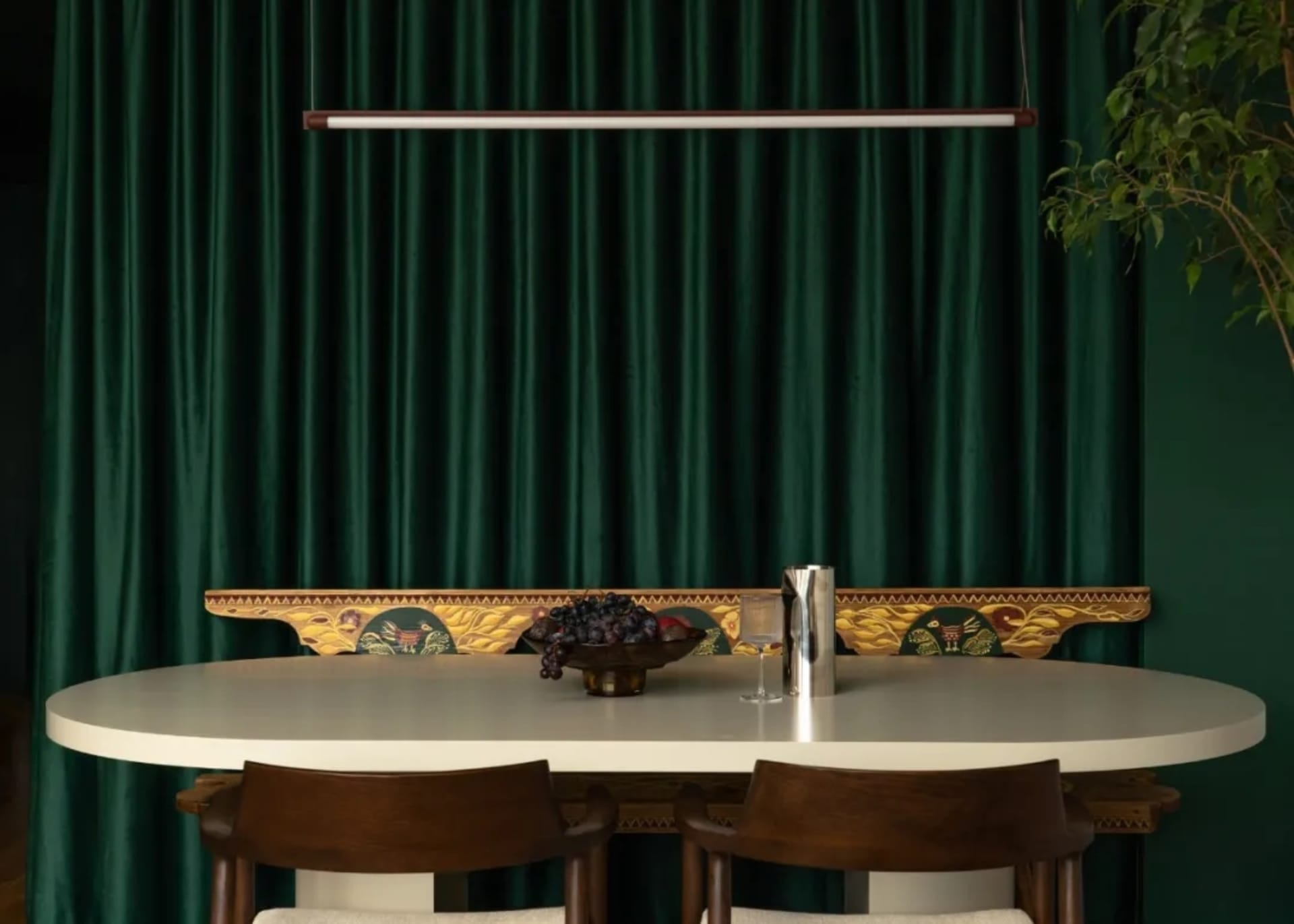 Dining room with a white table and chairs, surrounded by green curtains, and a bowl of fruit on the table, with soft and inviting lighting