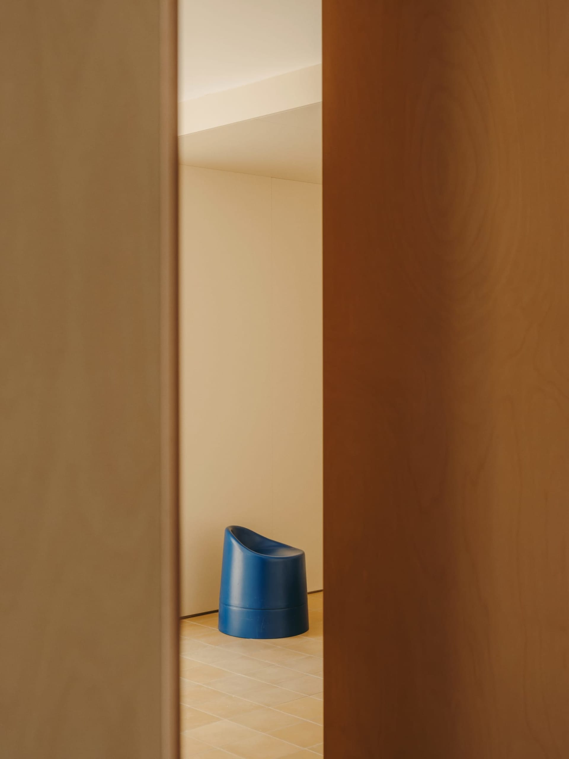 A small, white room with a blue chair near the door and a blue trash can in the center, creating a minimalist and clean atmosphere
