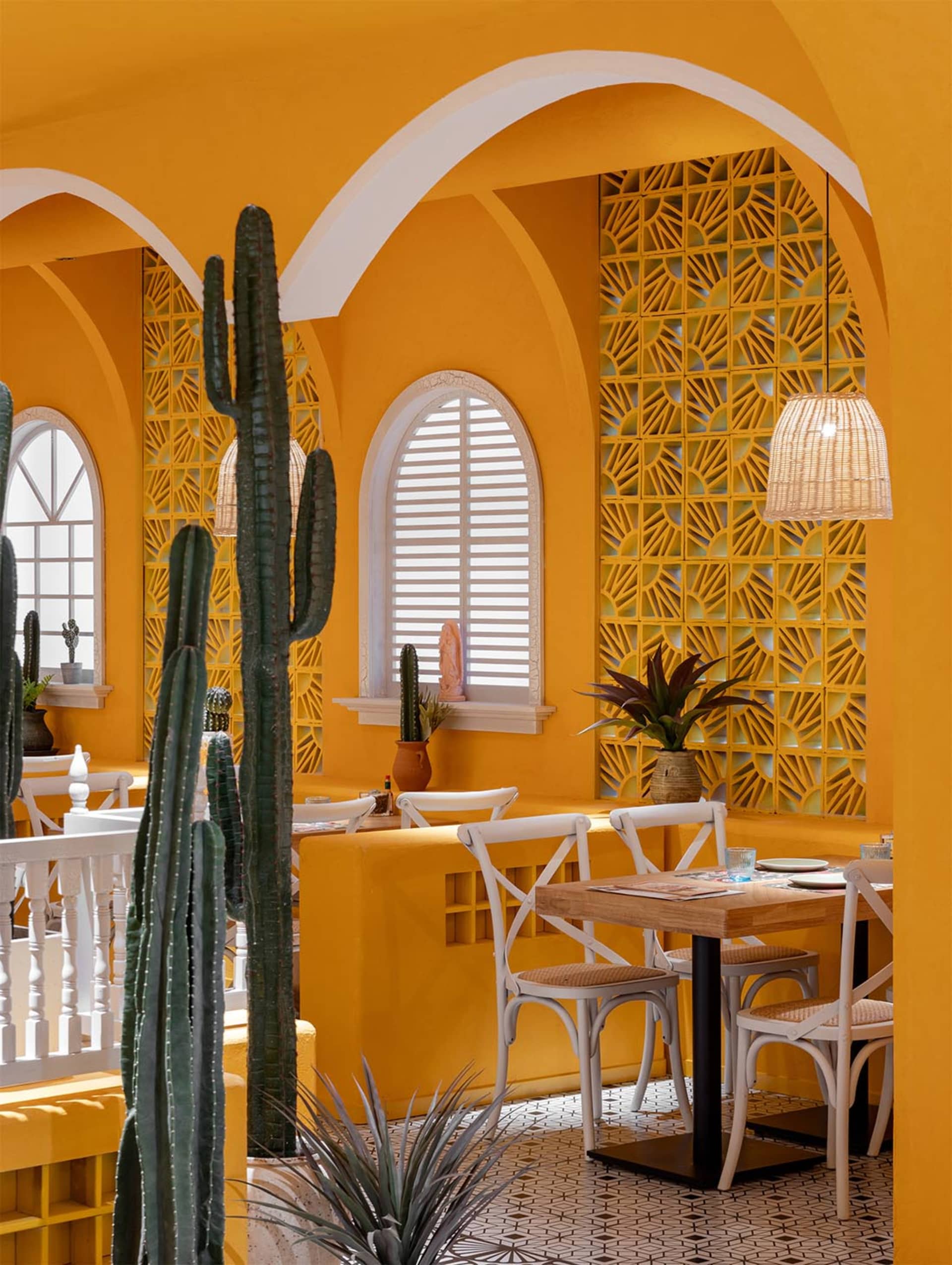 A warm and inviting restaurant with yellow walls, white furniture, and a large cactus in the dining area, surrounded by soft natural light