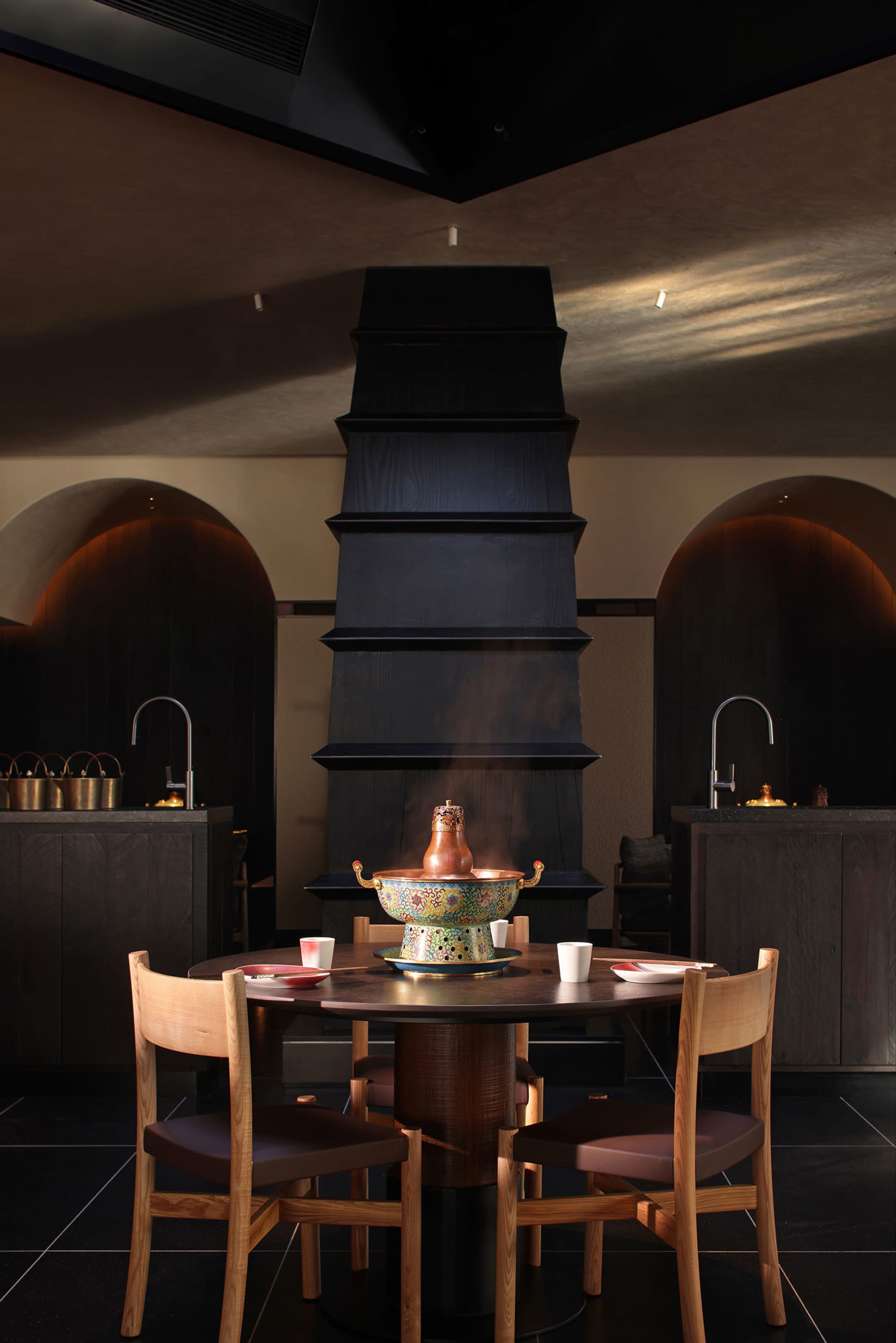 Cozy dining room with a table, chairs, and a black tower or chimney, set for a meal with cups, bowls, and a vase