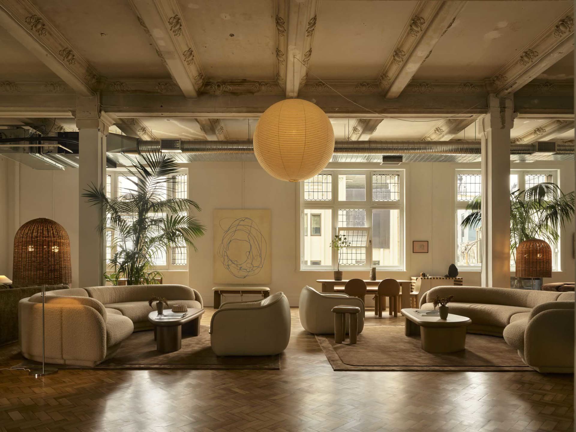 A large, open living room with a high ceiling, wood and glass materials, and natural light from the windows, featuring furniture, potted plants, and a modern design