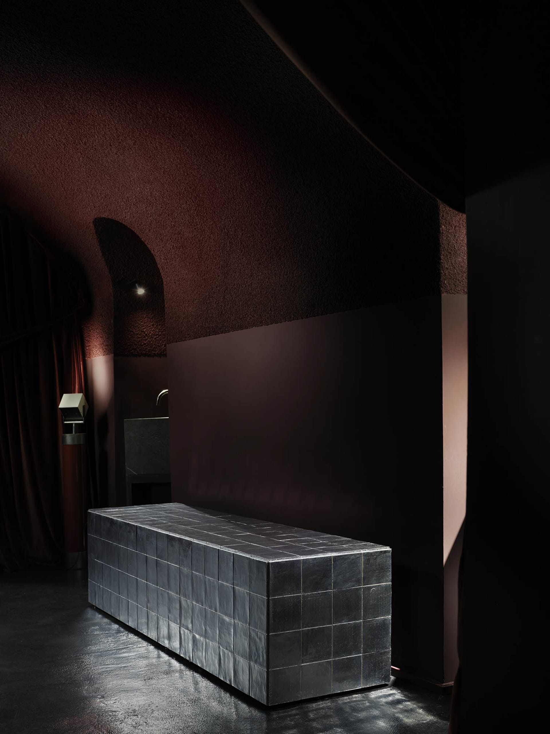 A small, dark room with a metal bench against a red wall, creating a moody and intimate atmosphere