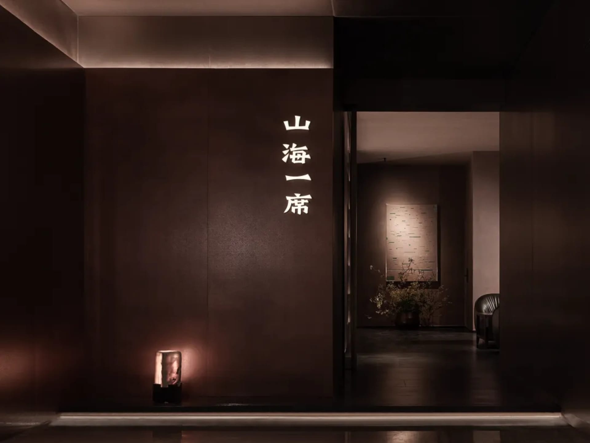 擺滿了中國字的紅色牆壁走廊，裡面放著一盆植物，還有昏黃的燈光