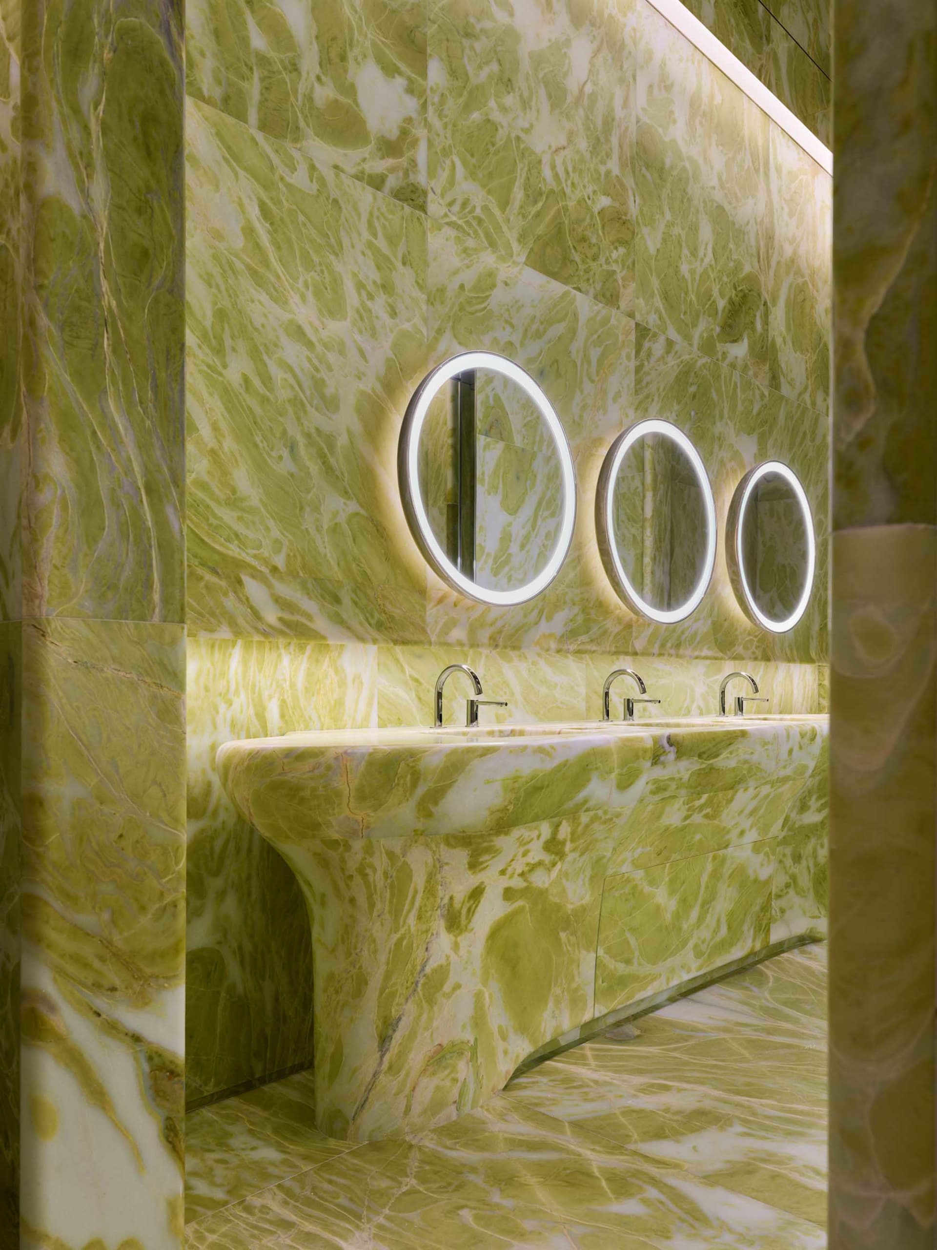 A well-lit bathroom with a green marble sink, a mirror above it, and three additional mirrors, creating a sense of luxury and sophistication