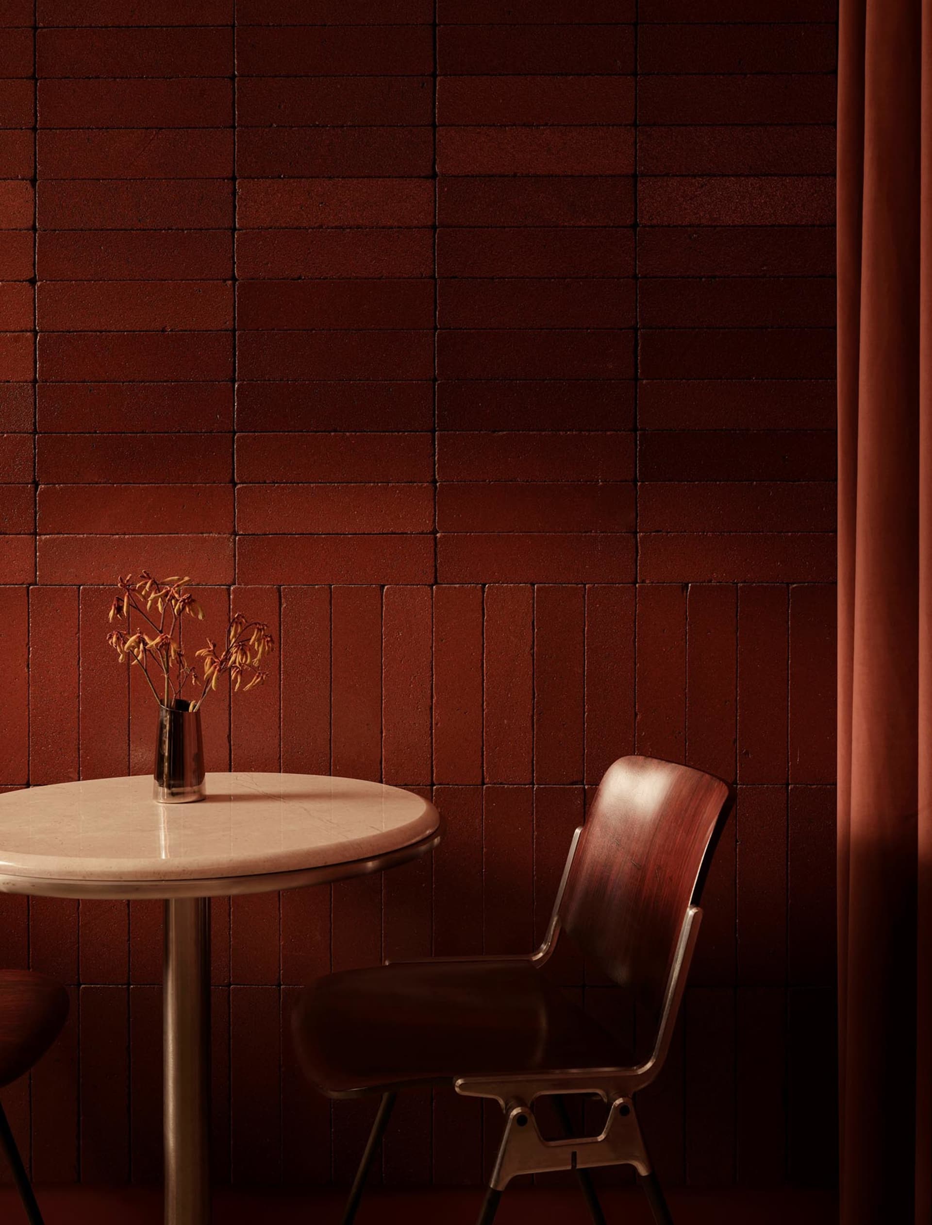 Dining area with a marble table and wooden chairs, surrounded by a brick wall, with a vase and flowers on the table, in a dimly lit space