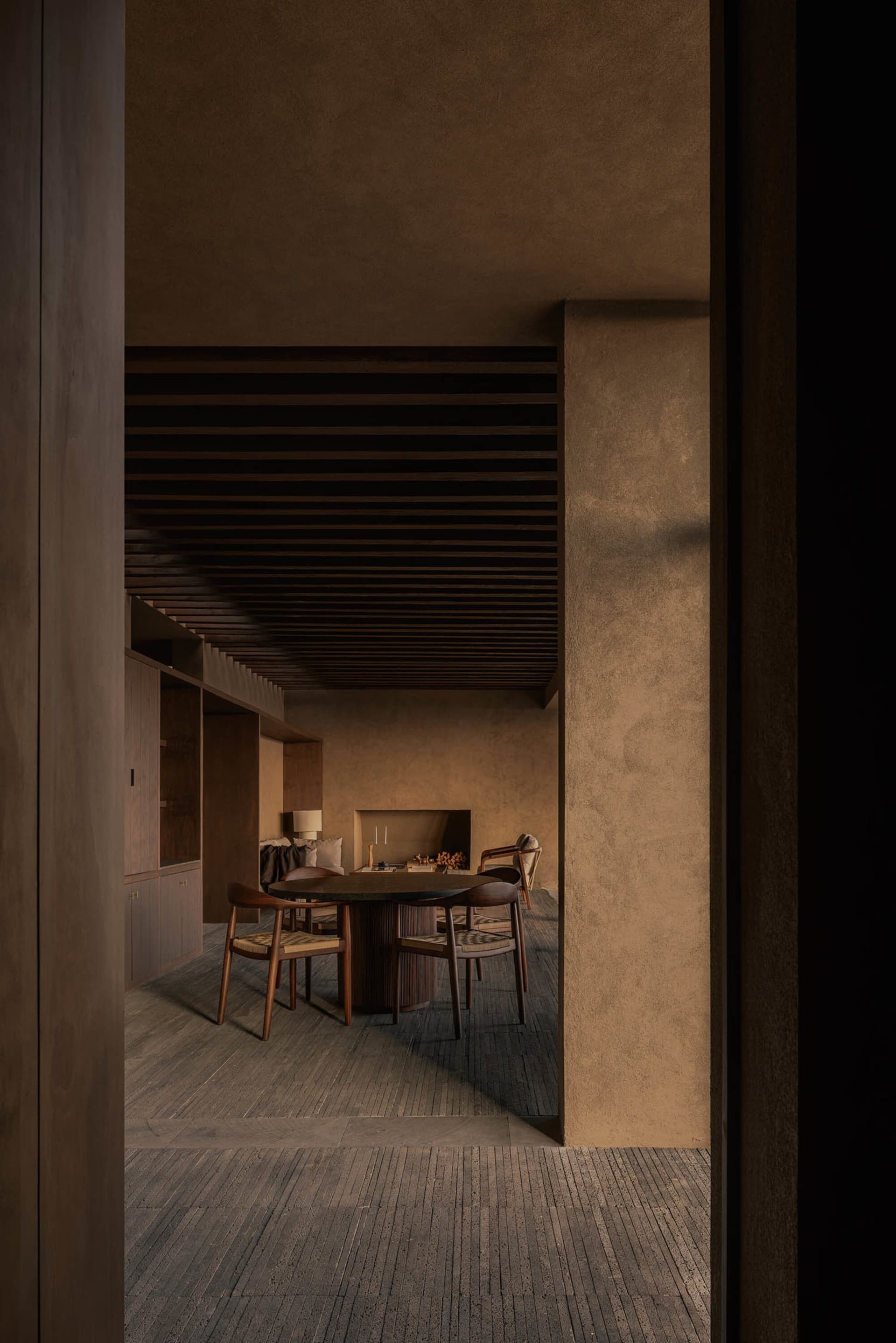 Cozy living room with a wooden floor, stone wall, and a dining table surrounded by chairs, lit by dim lighting