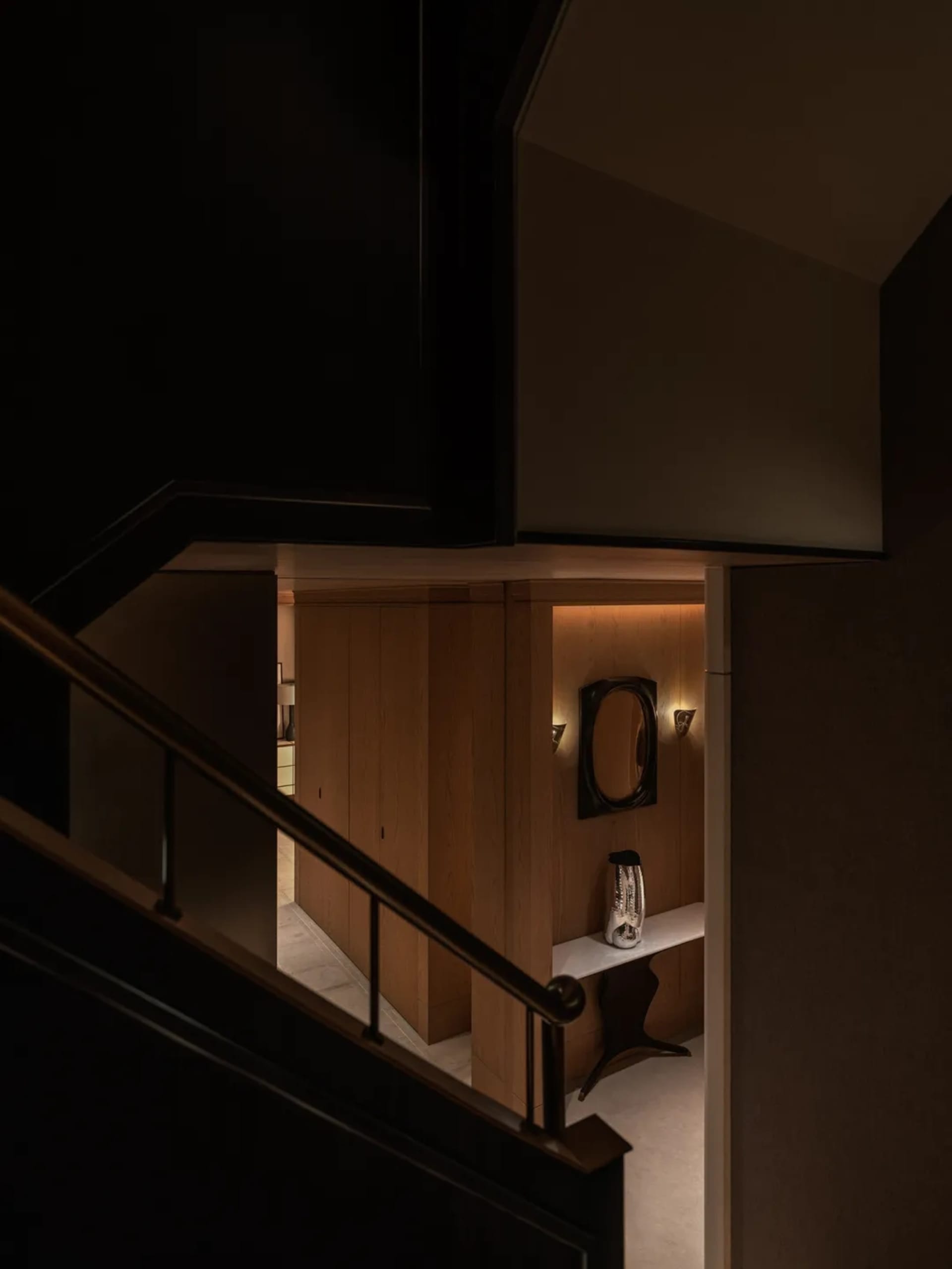 A dimly lit stairwell with a wooden staircase and metal railing, creating a mysterious atmosphere