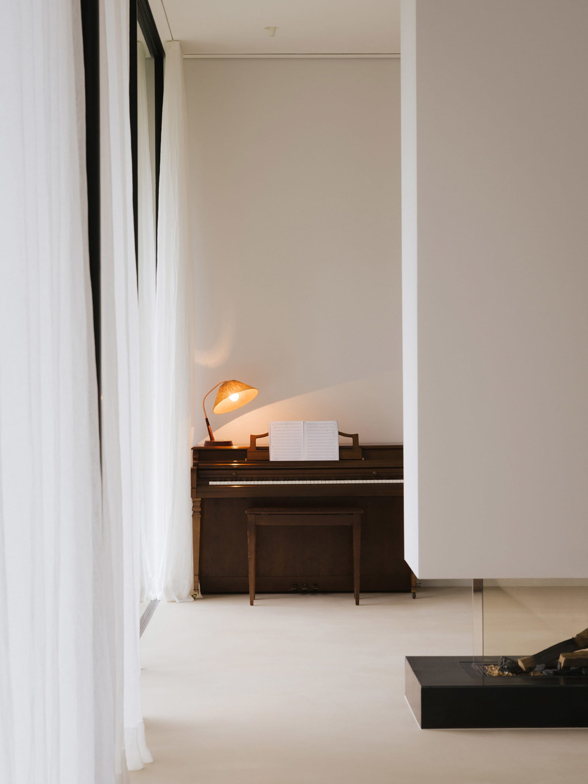 Cozy living space with a piano and fireplace, featuring a white color scheme and a brown piano, with a warm and inviting atmosphere
