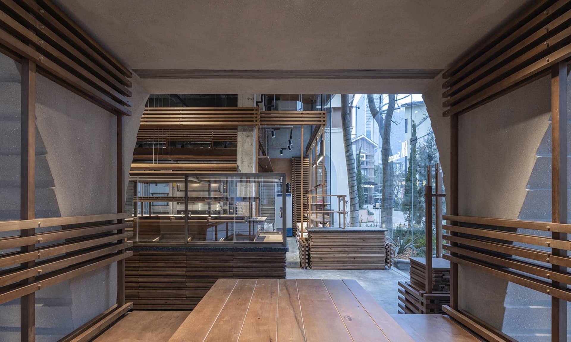 A warm and inviting restaurant interior with a large wooden dining table, wooden chairs, and a wooden counter, surrounded by natural lighting
