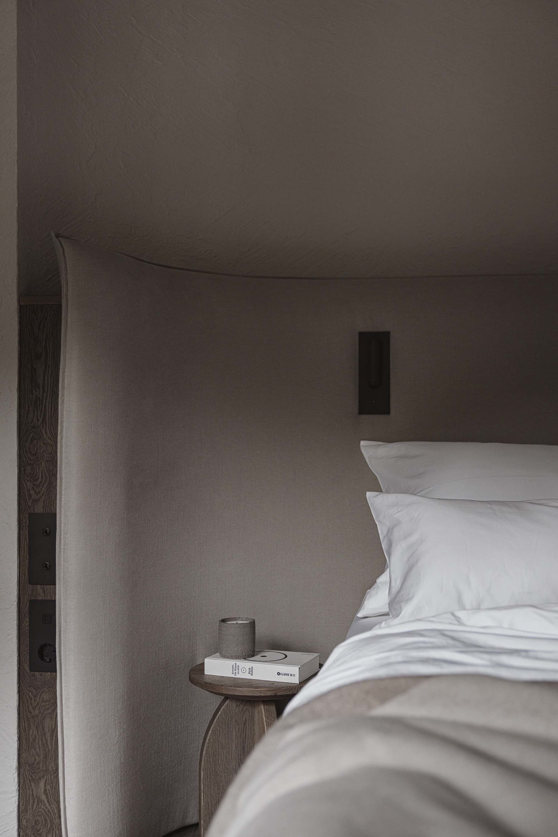 Cozy bedroom with a wooden bed, nightstand, and floor, dimly lit with a lamp and a book on the nightstand
