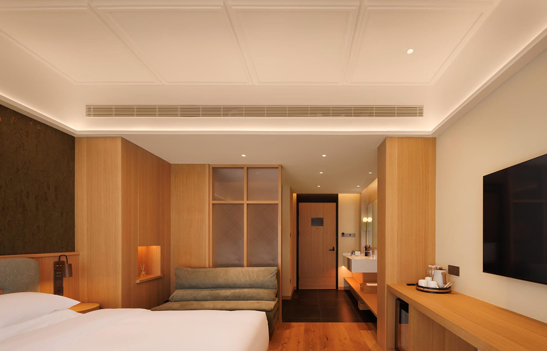 Cozy bedroom with a bed, couch, and mirror, surrounded by wooden furniture and a wooden floor, in a well-lit space