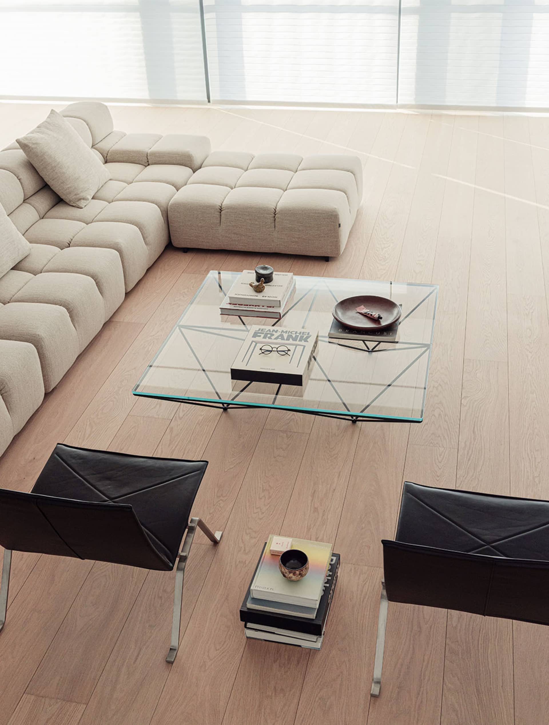 A living room with a large couch, glass coffee table, and bookshelf, featuring a clean and modern appearance with a wooden floor and predominantly white furniture