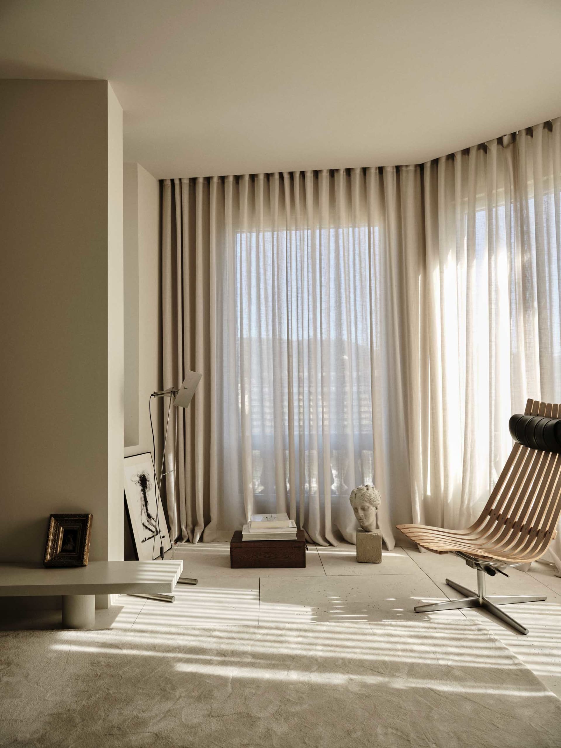 A modern living room with a large window, a couch, chair, dining table, and bookshelf, all in a predominantly white space with natural light