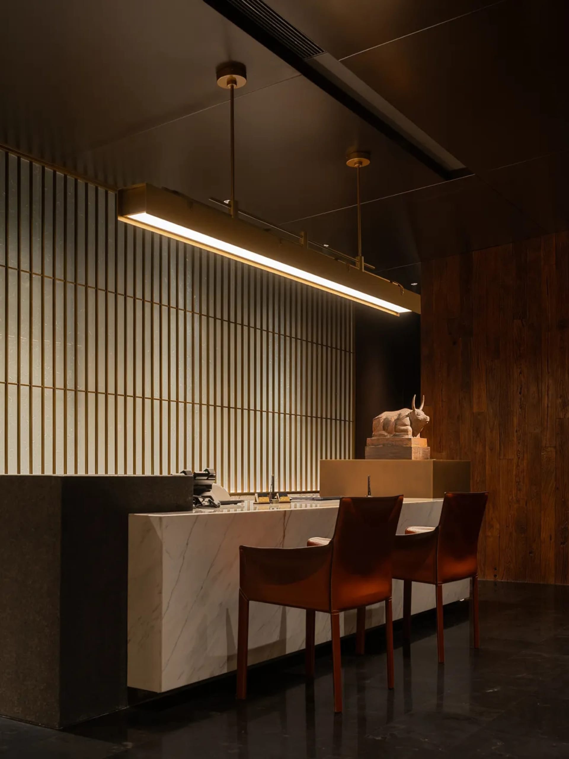 Modern kitchen with a dining table, chairs, and a vase, featuring marble countertops, wood flooring, and a dimly lit atmosphere