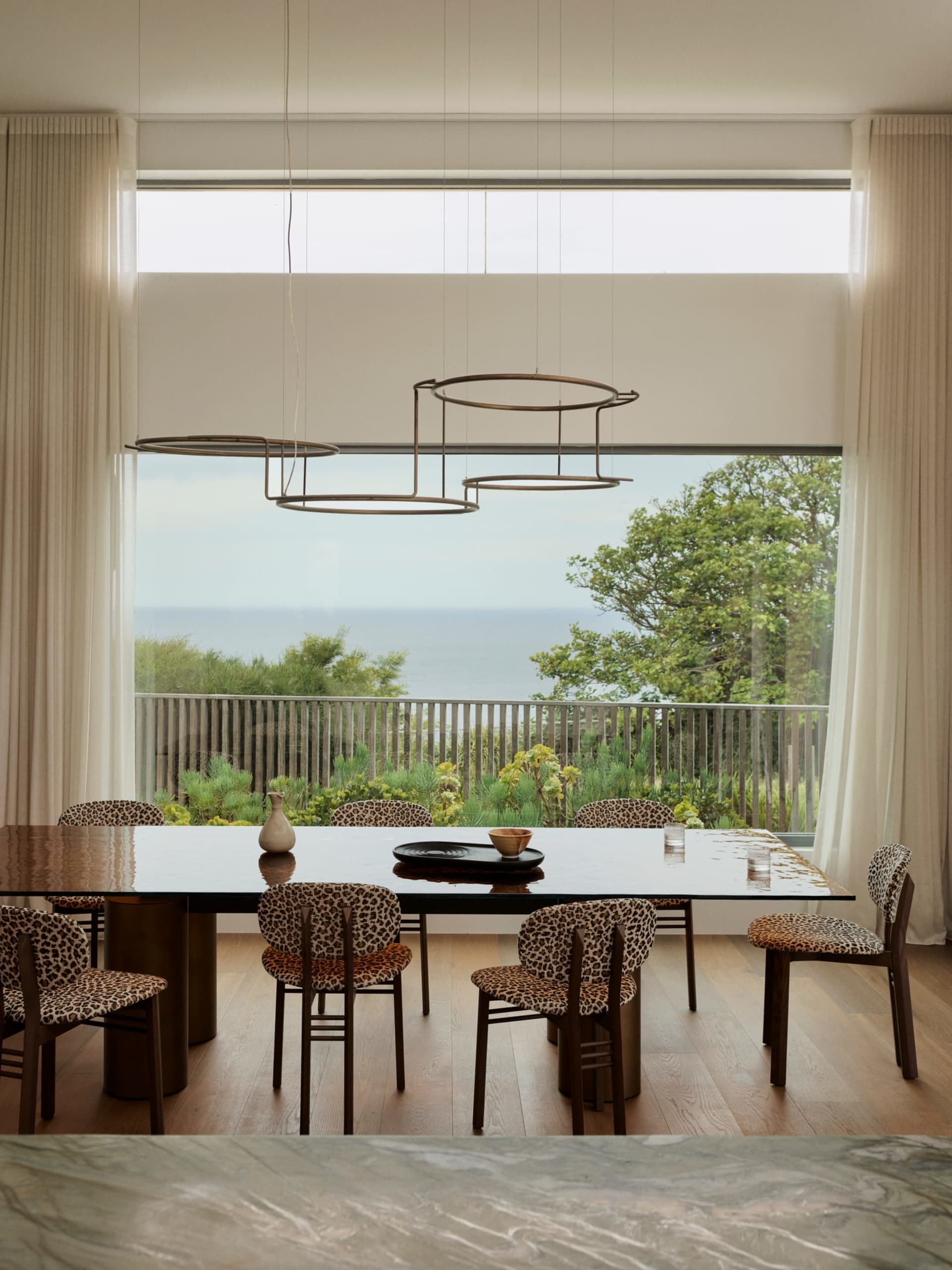 Dining room with a large wooden table and chairs, set with various items, surrounded by a large window with natural light