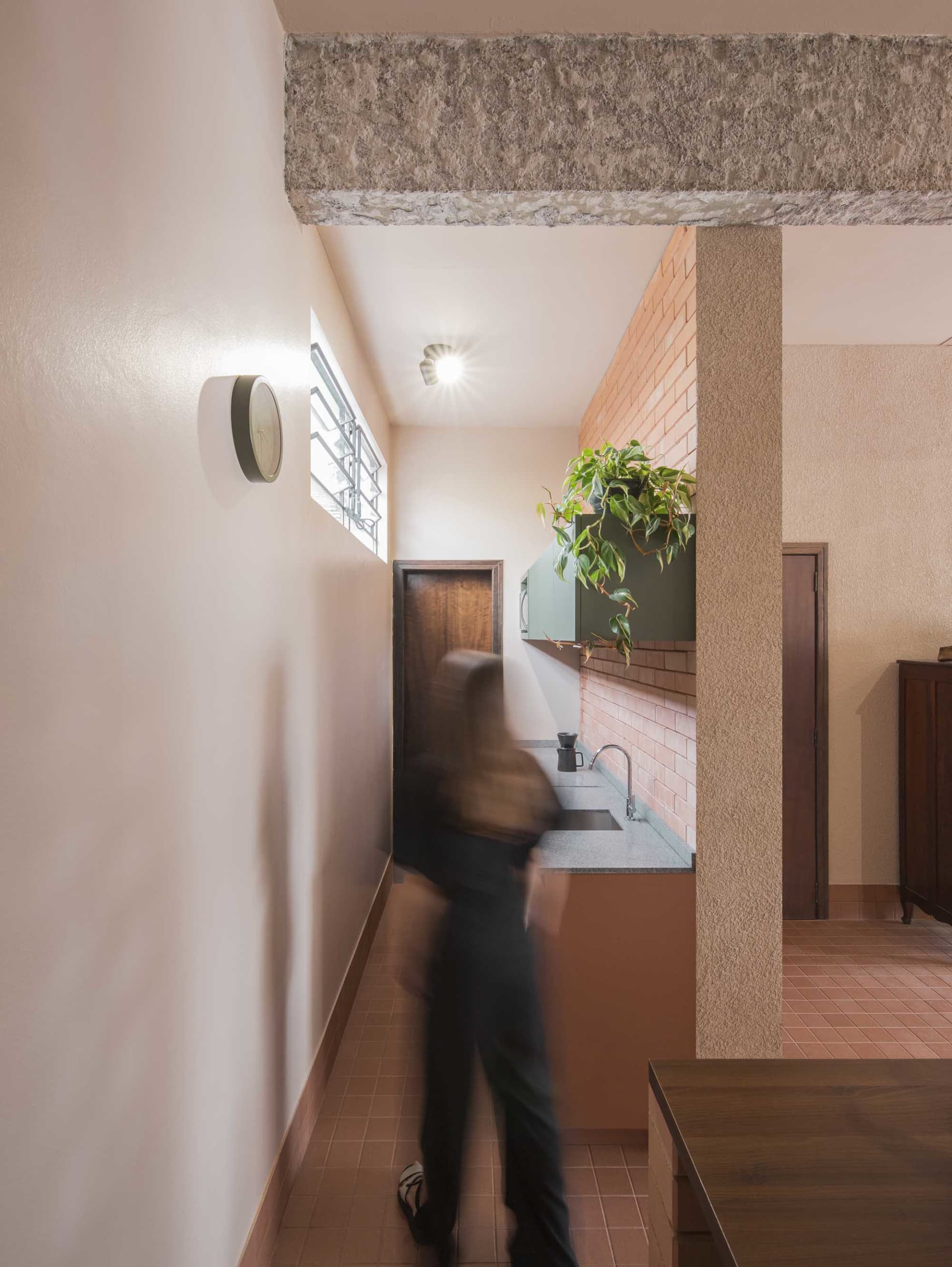 A woman walks towards the sink in a kitchen with a potted plant and a vase, surrounded by everyday objects and casual decor