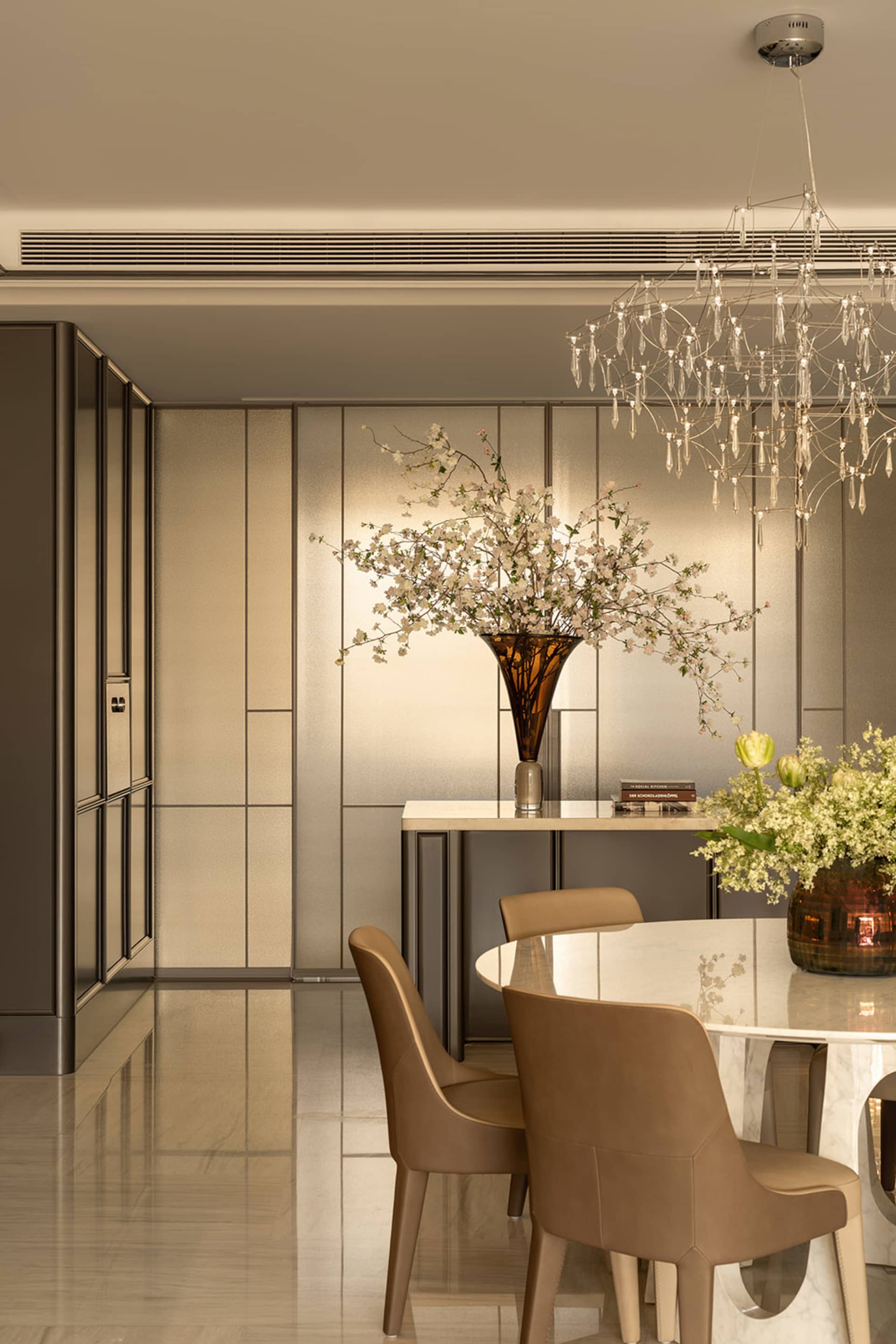 A modern living room with a dining table, chairs, and a vase of flowers, surrounded by a large window and wood and glass materials, creating a warm and inviting atmosphere