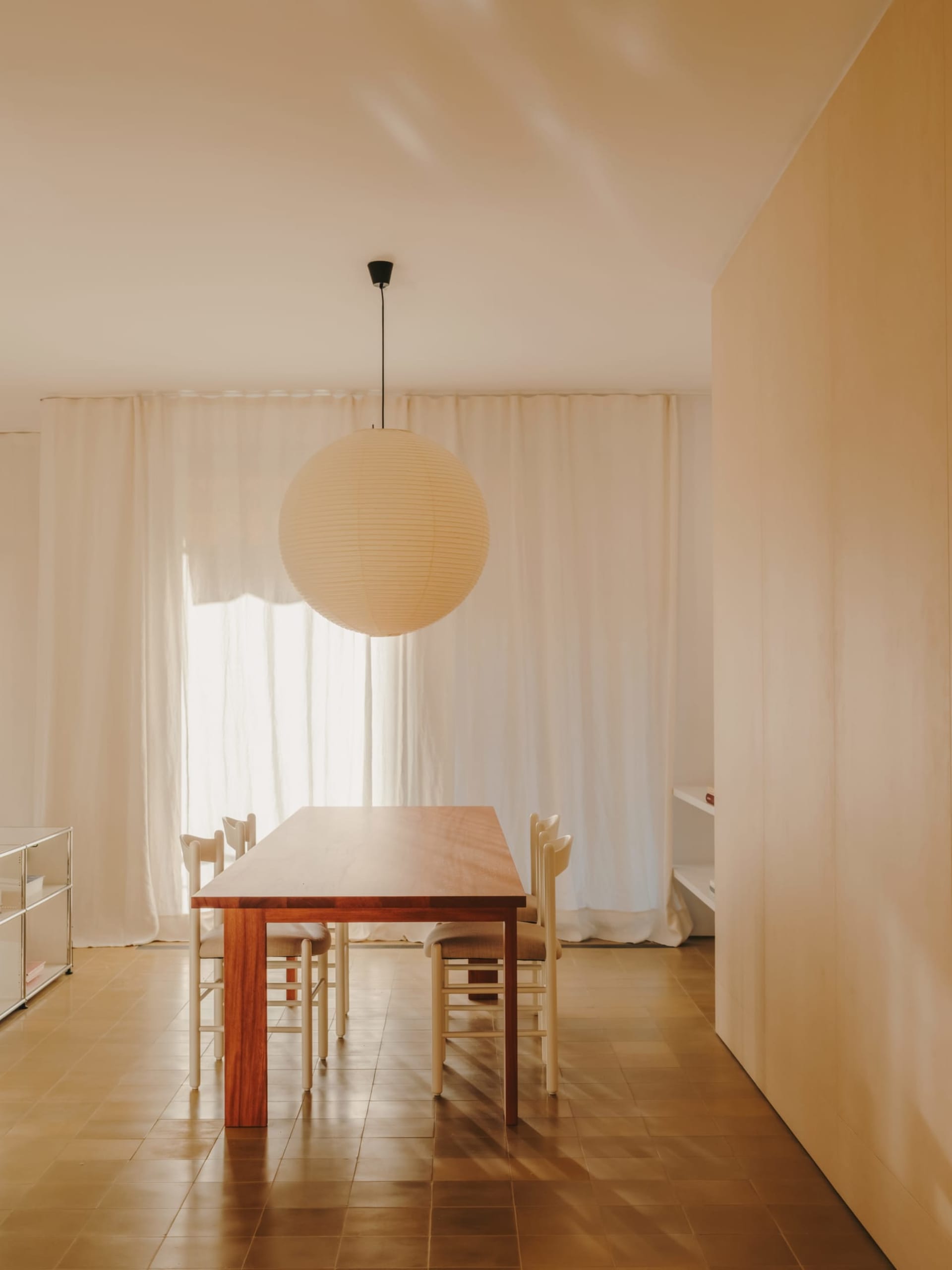 Dining room with a wooden table and chairs, surrounded by a modern and minimalistic space with natural light and a warm atmosphere