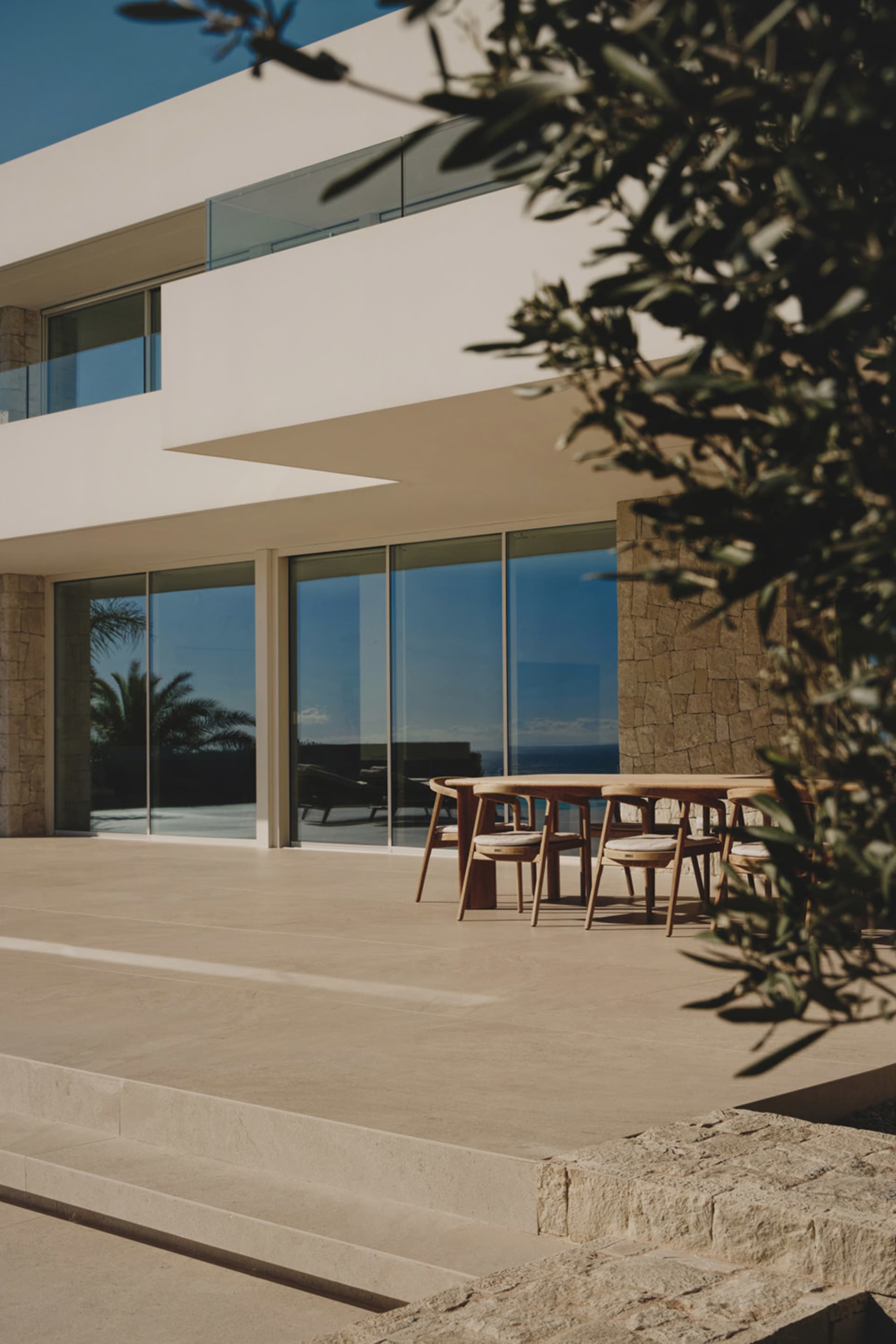 A modern house with a patio area featuring a glass door, large window, and comfortable outdoor seating with a dining table and chairs, surrounded by natural light and visually appealing materials