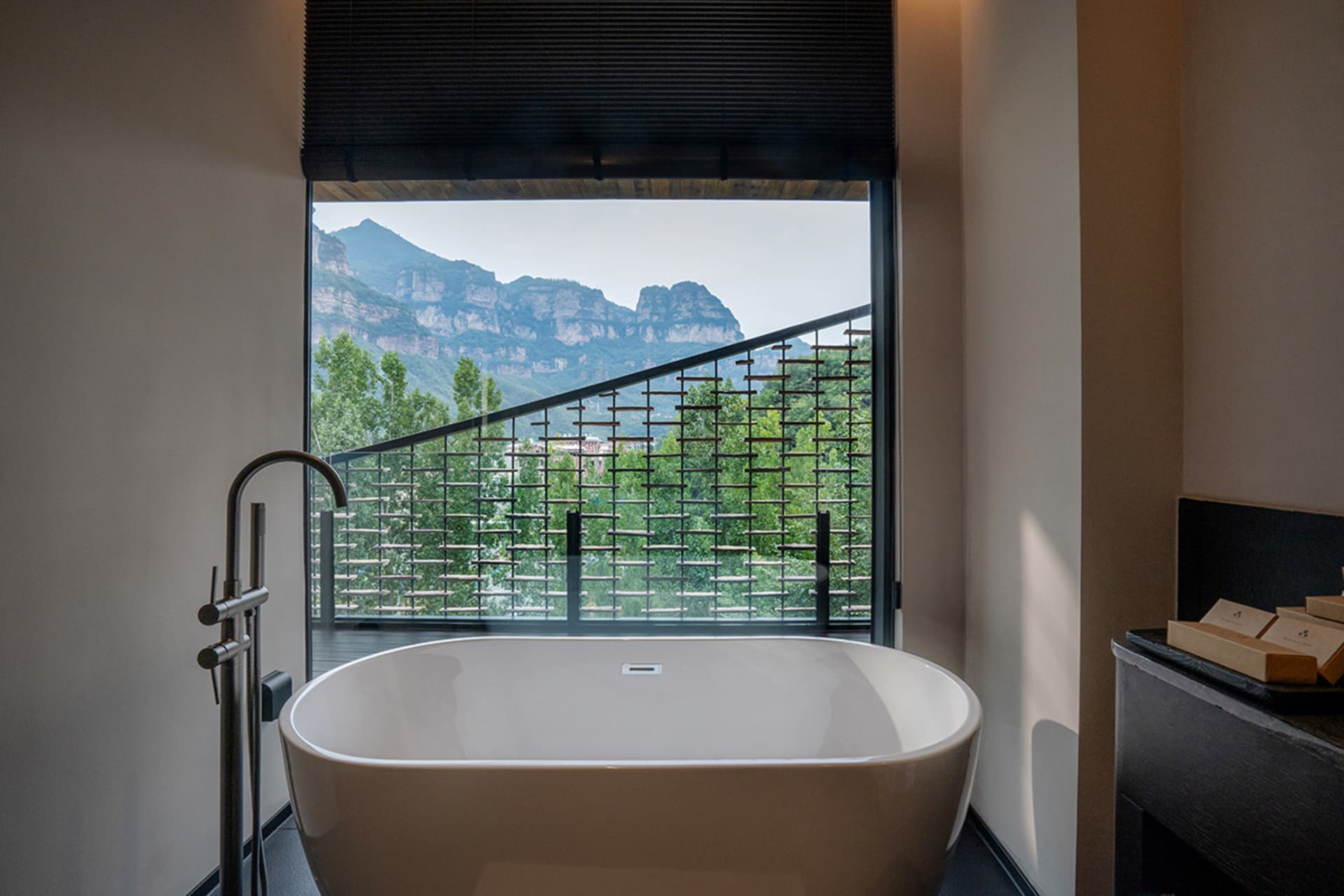 A serene bathroom with a white bathtub, black railing, and a large window offering a breathtaking mountain view