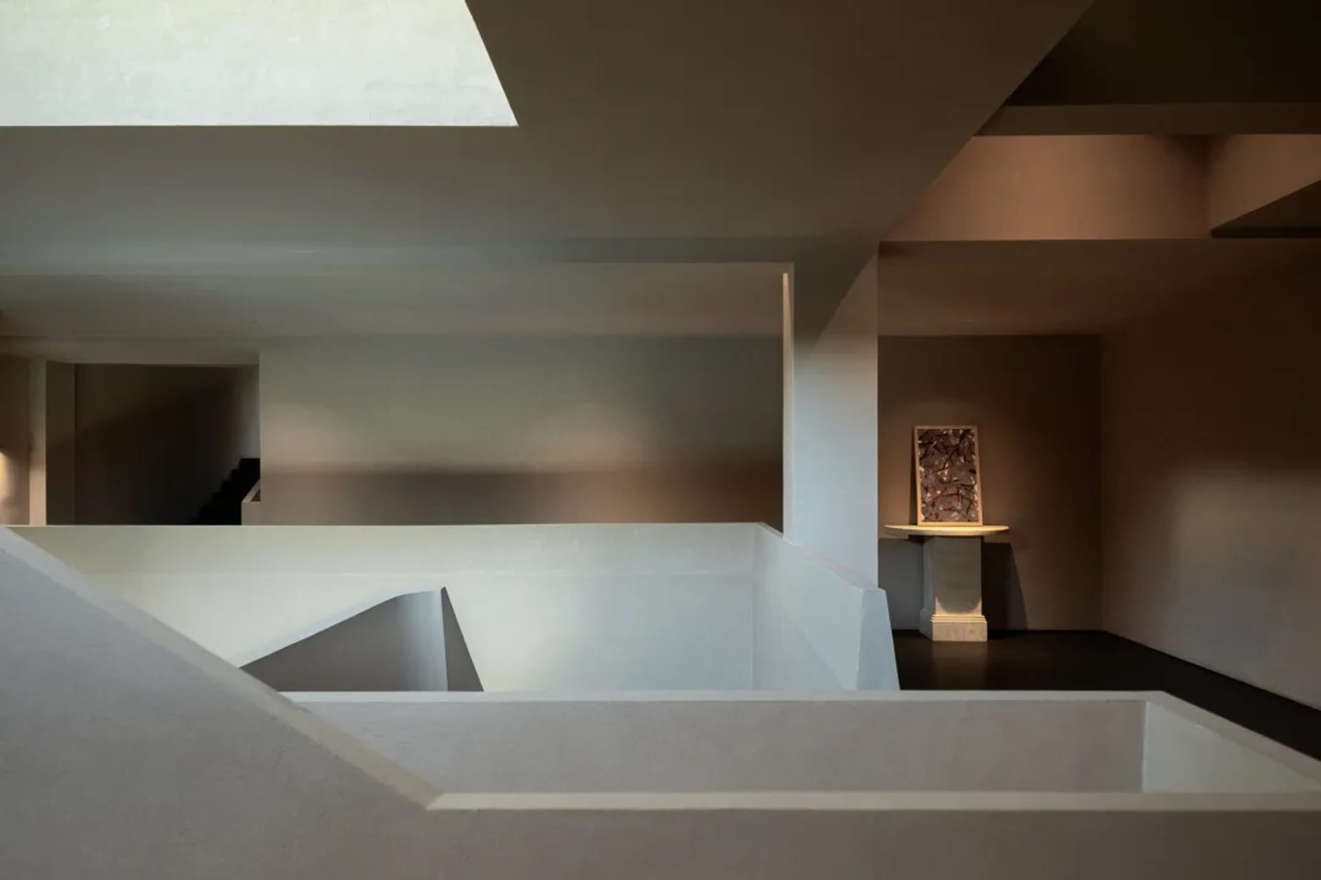 A modern art gallery with a white wall, a large window, and a painting displayed near the center of the wall, with natural light streaming in