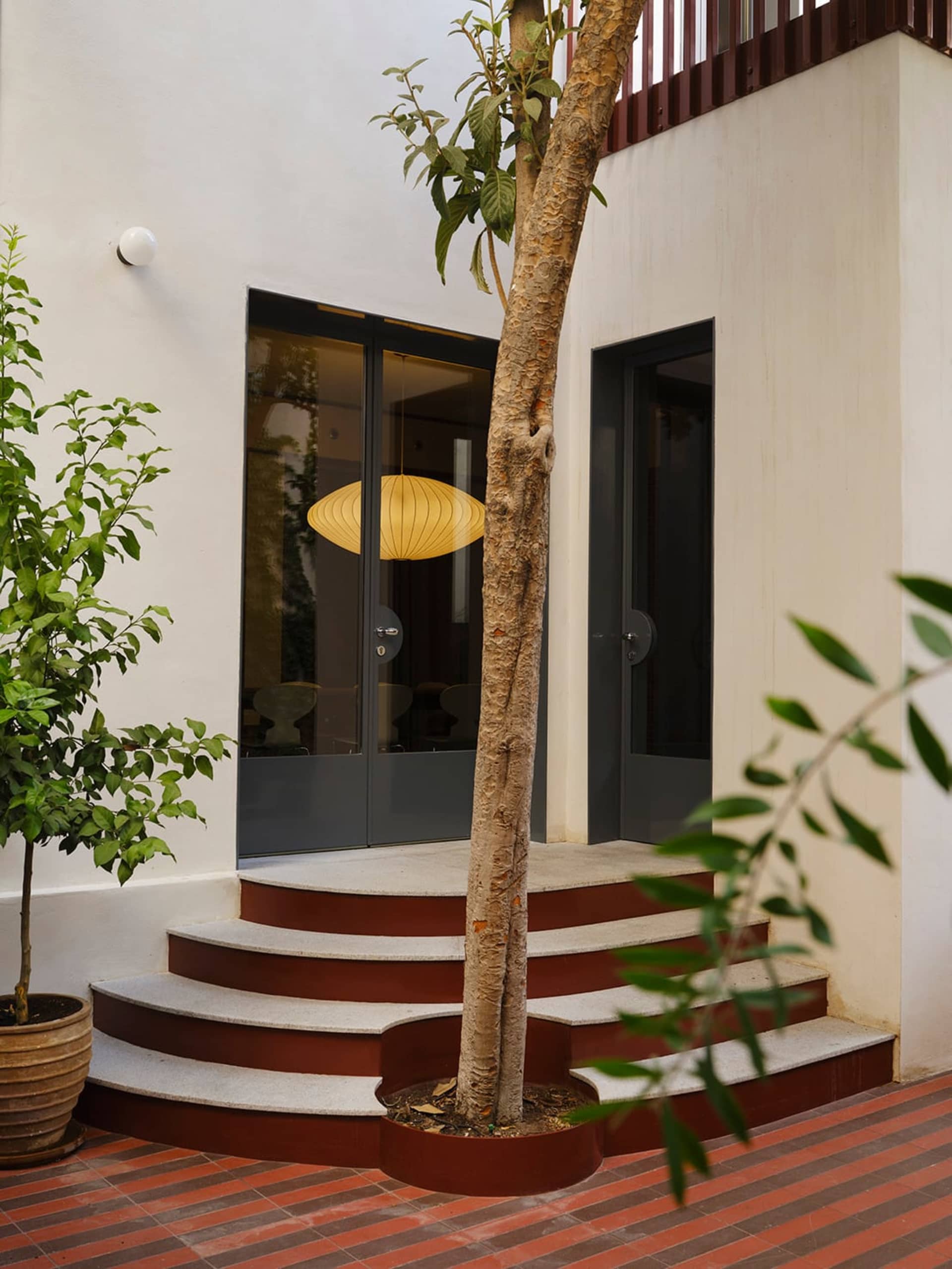 一座現代式家庭住宅，外牆以混凝土建造，內部則以木頭 staircase 裝飾，置於自然的戶外環境中，氛圍悠閒、溫馨