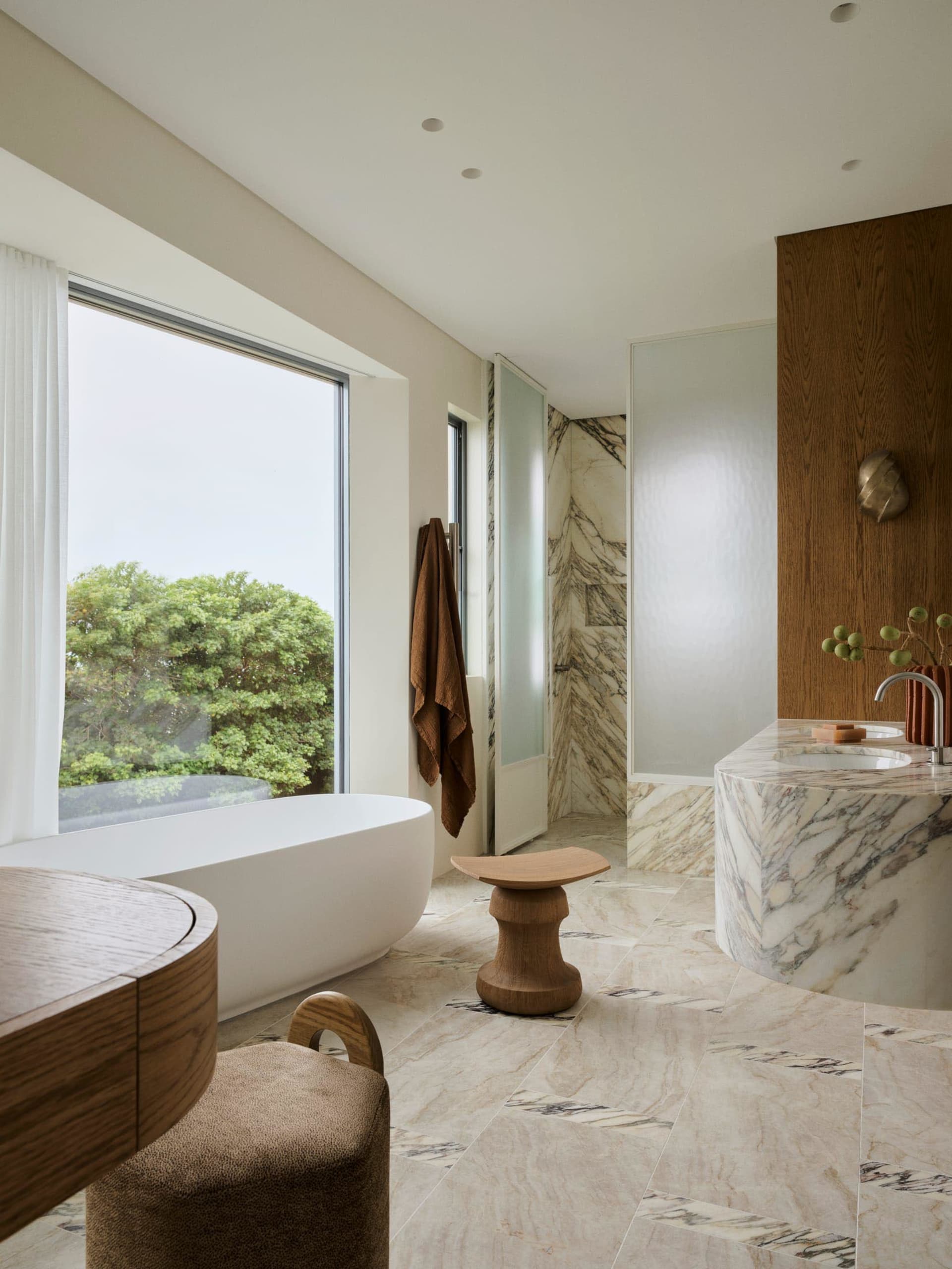 Luxurious bathroom with a marble-tiled floor, a large bathtub, sink, and toilet, well-lit and modern in style