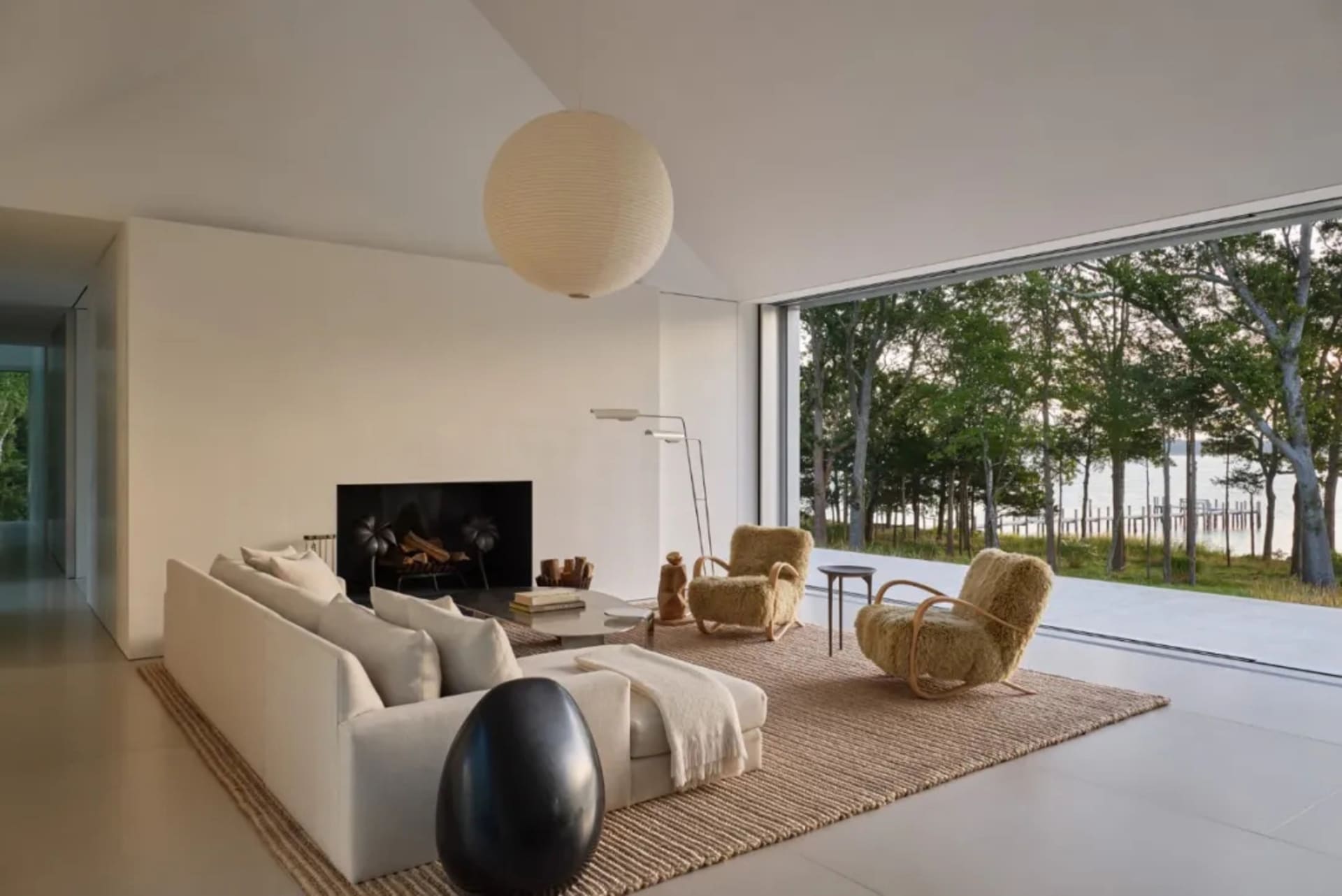 Cozy modern living room with a white couch, a chair, and a fireplace, surrounded by natural light from a large window