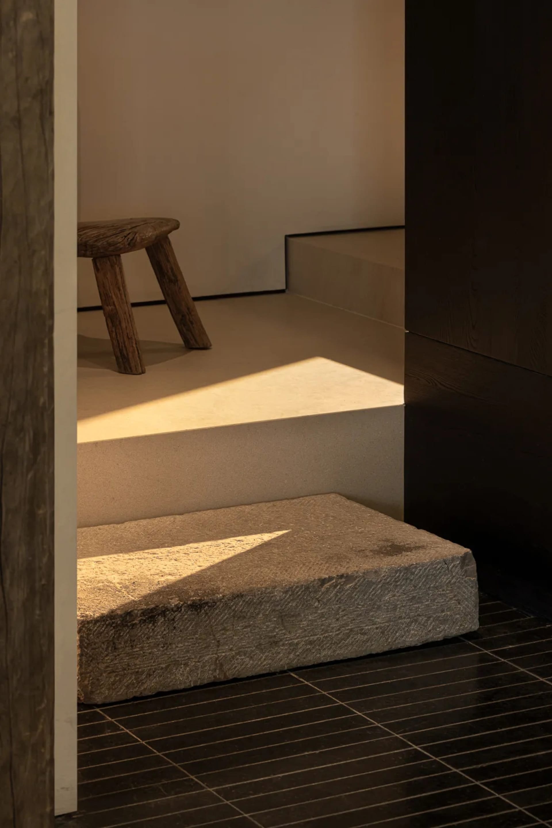 Cozy living room with a wooden staircase and stone bench, natural light from a window, and warm wood and stone materials