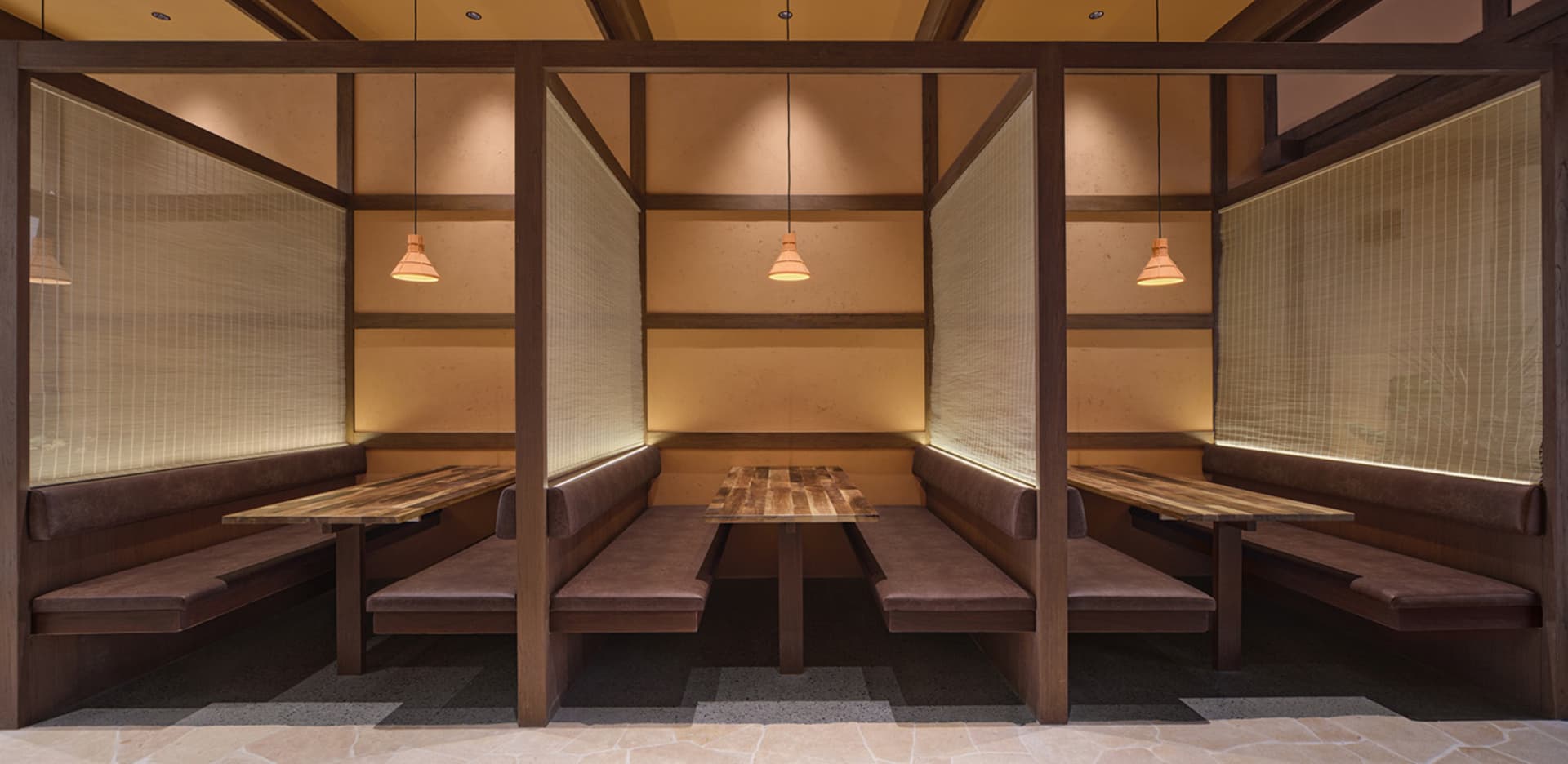 Rustic dining space with wooden benches, cushions, and a dining table, illuminated by a series of lights