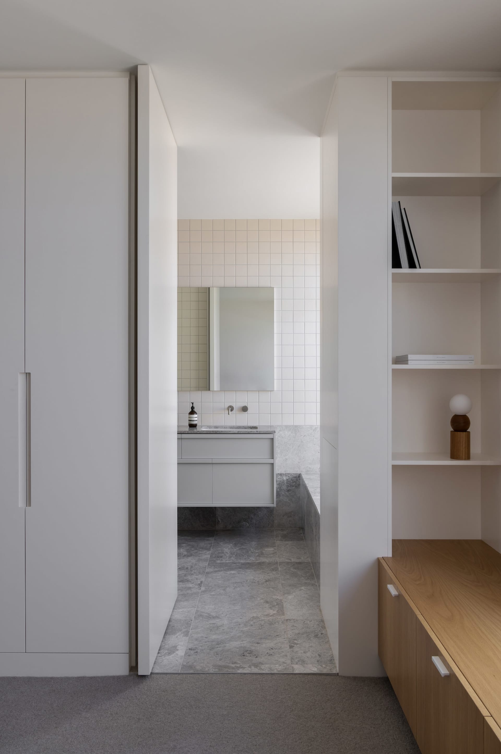 A modern bathroom with a white sink, mirror, and cabinet, well-lit by natural light from a window