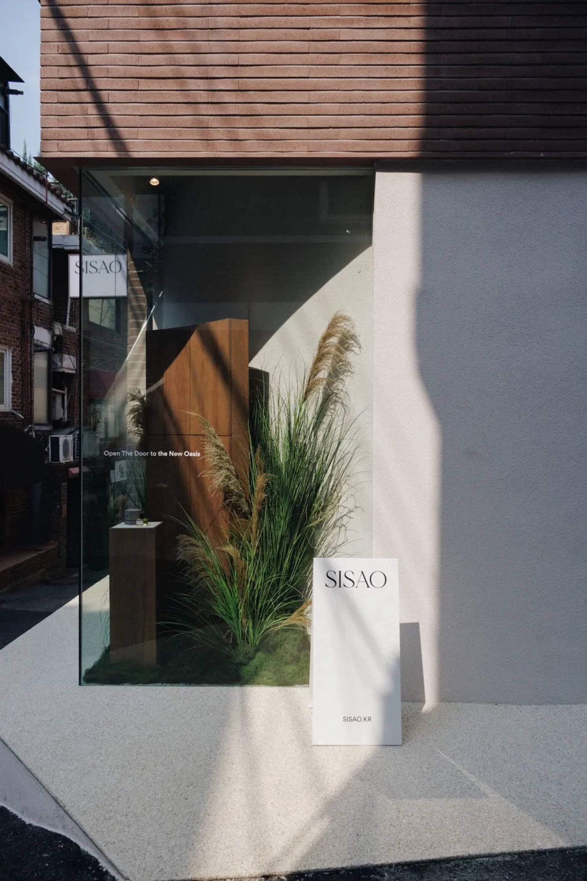 A storefront with a display of plants and a sign, featuring a glass door and window, with natural light and a modern appearance