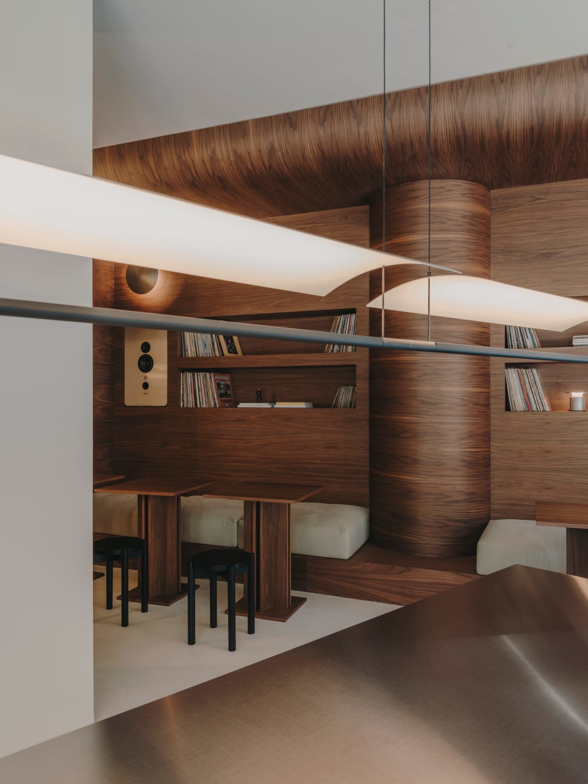 A dimly lit room with wooden walls and floors, featuring a dining table, bookshelf, and couch, creating a warm and cozy atmosphere