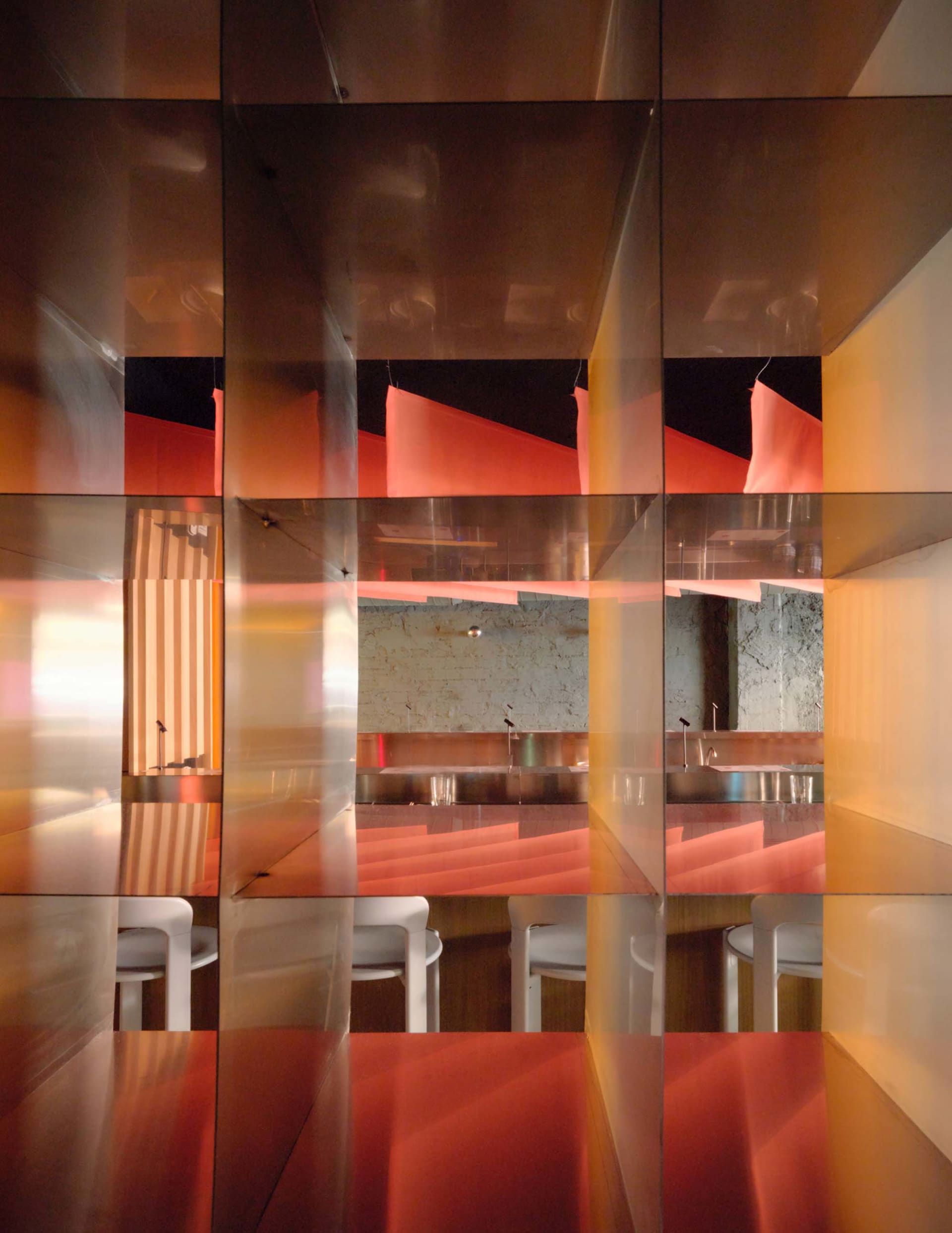 A modern restaurant interior with a wooden dining table surrounded by white chairs, a red accent wall, and dim lighting creating a cozy atmosphere