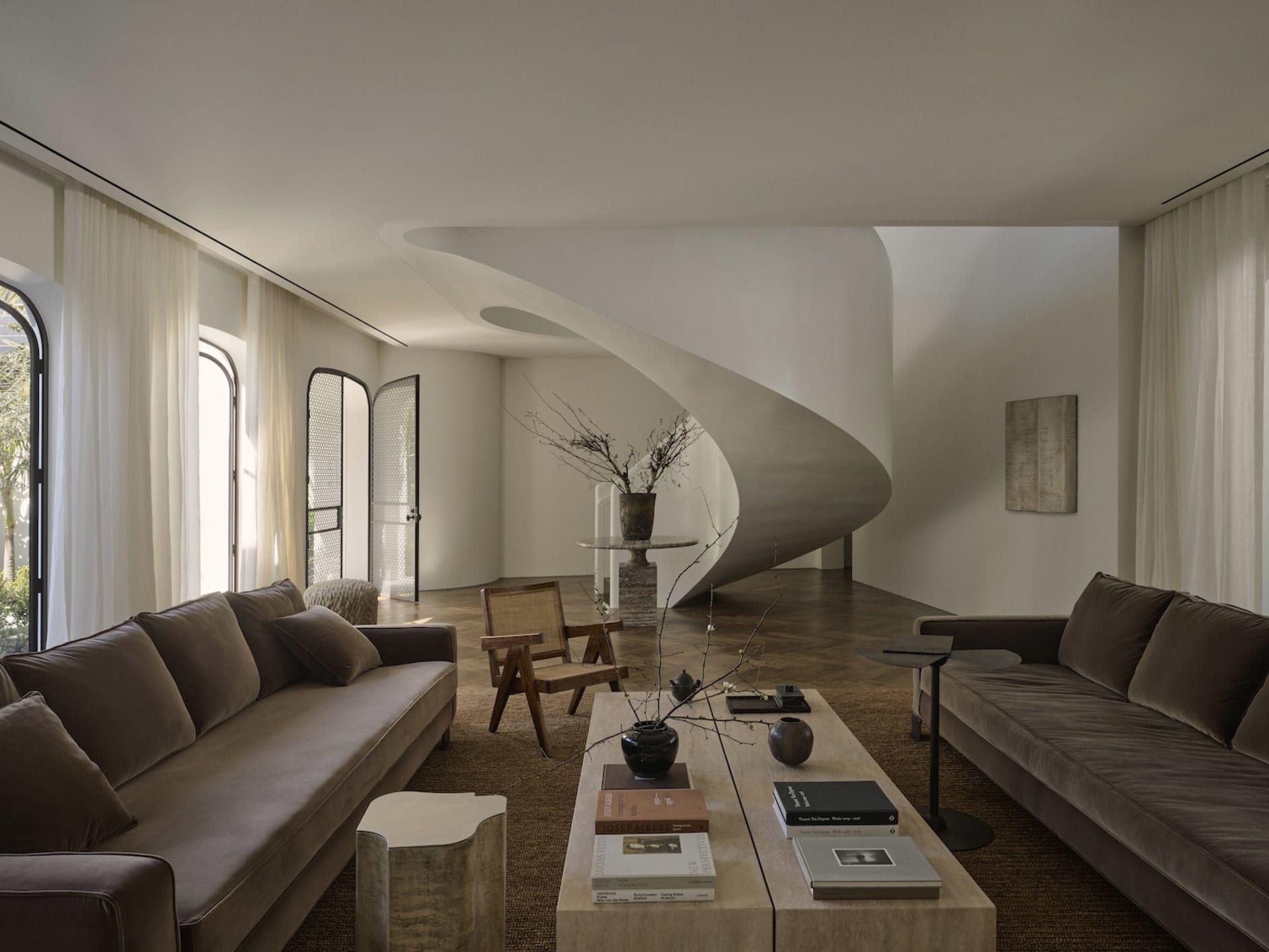Comfortable and inviting living space with a large couch, coffee table, and spiral staircase, surrounded by natural light and decorative elements