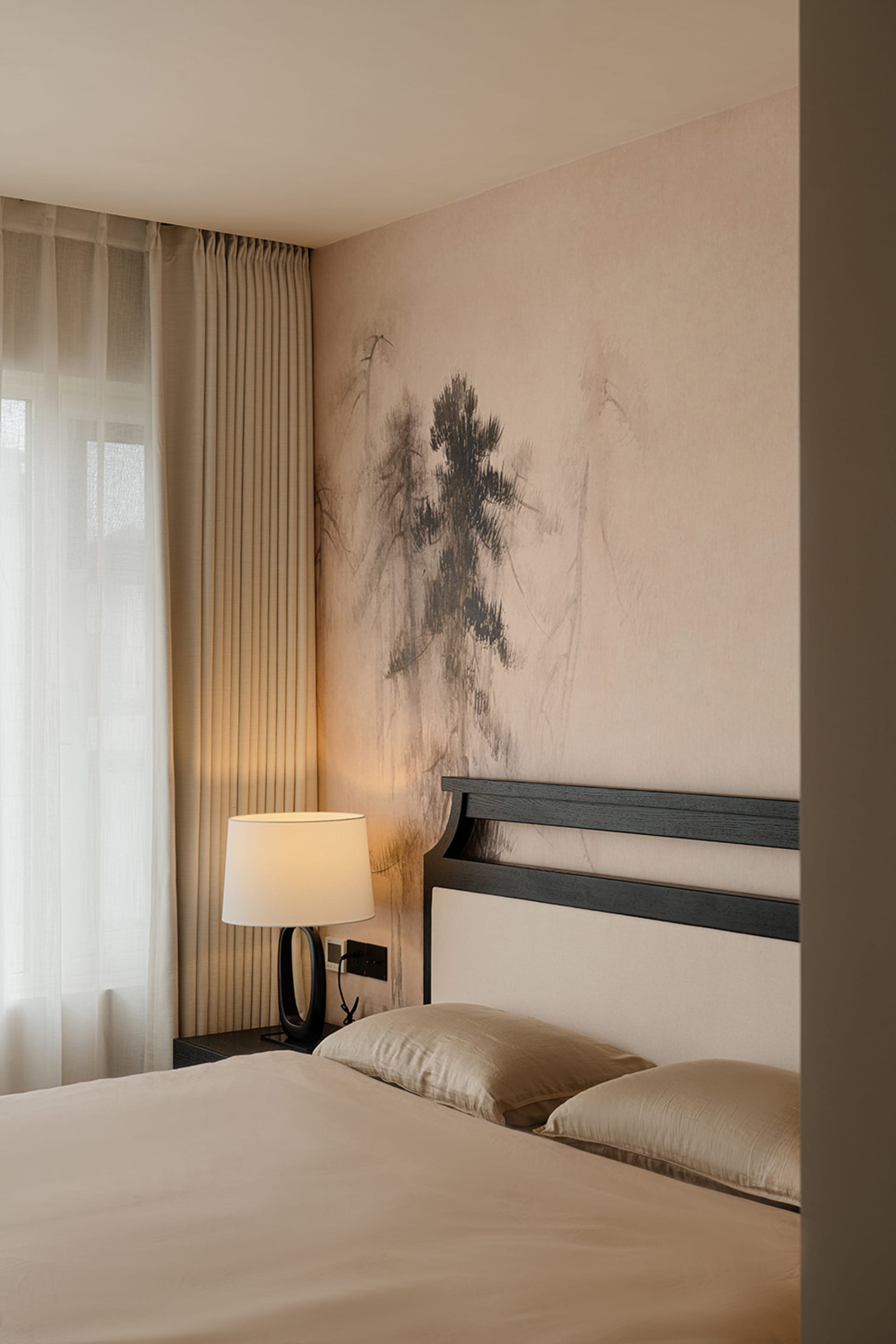A modern bedroom with a bed, a lamp, and a nature-inspired wall painting, featuring soft and warm lighting